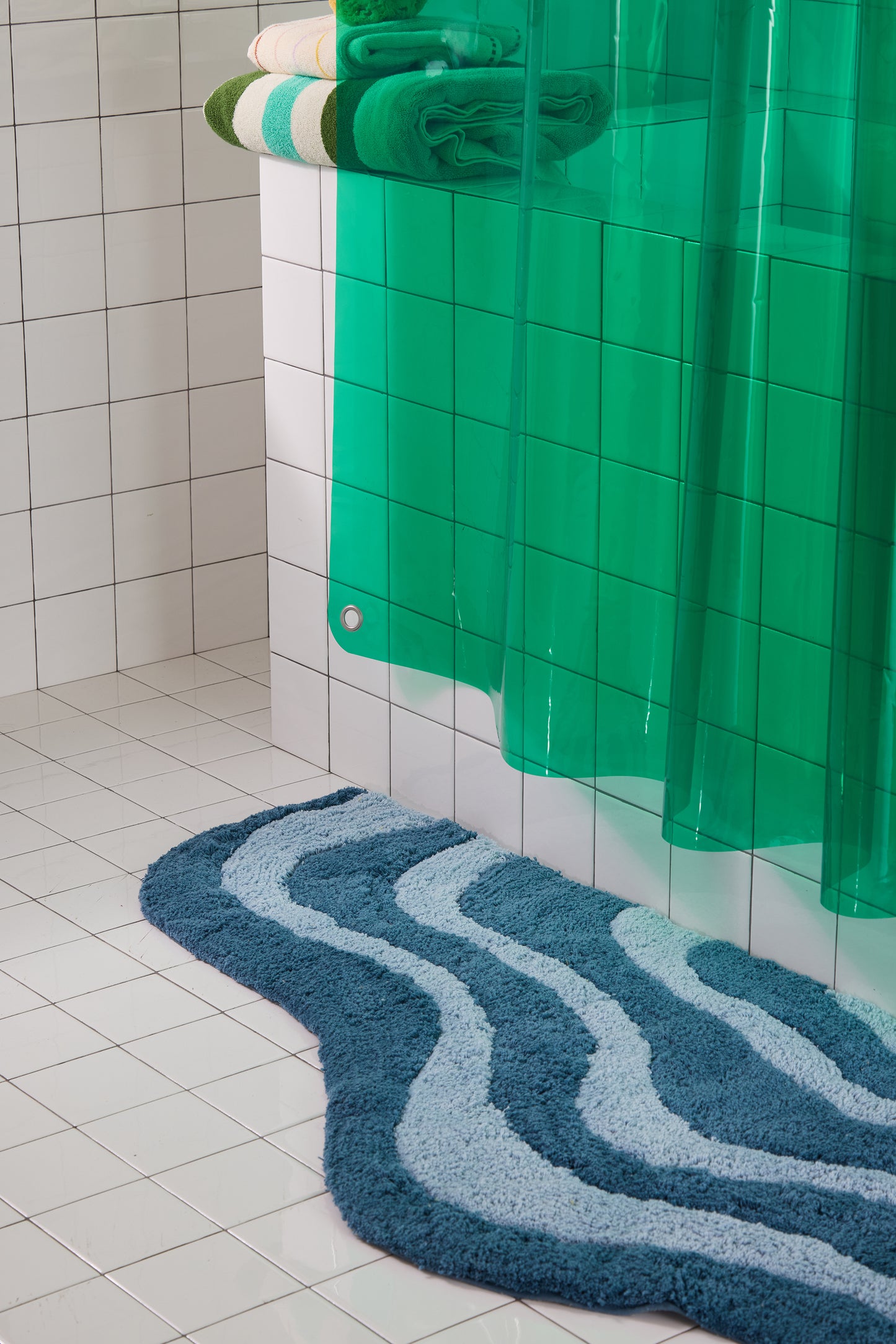 Bathroom with a green shower curtain and blue textured rug on a tiled floor.
