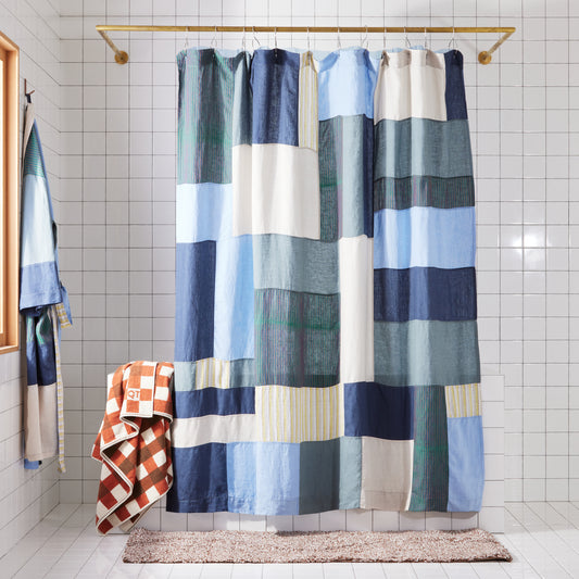 Multi-color blue shower curtain hanging in white tiled bathroom.