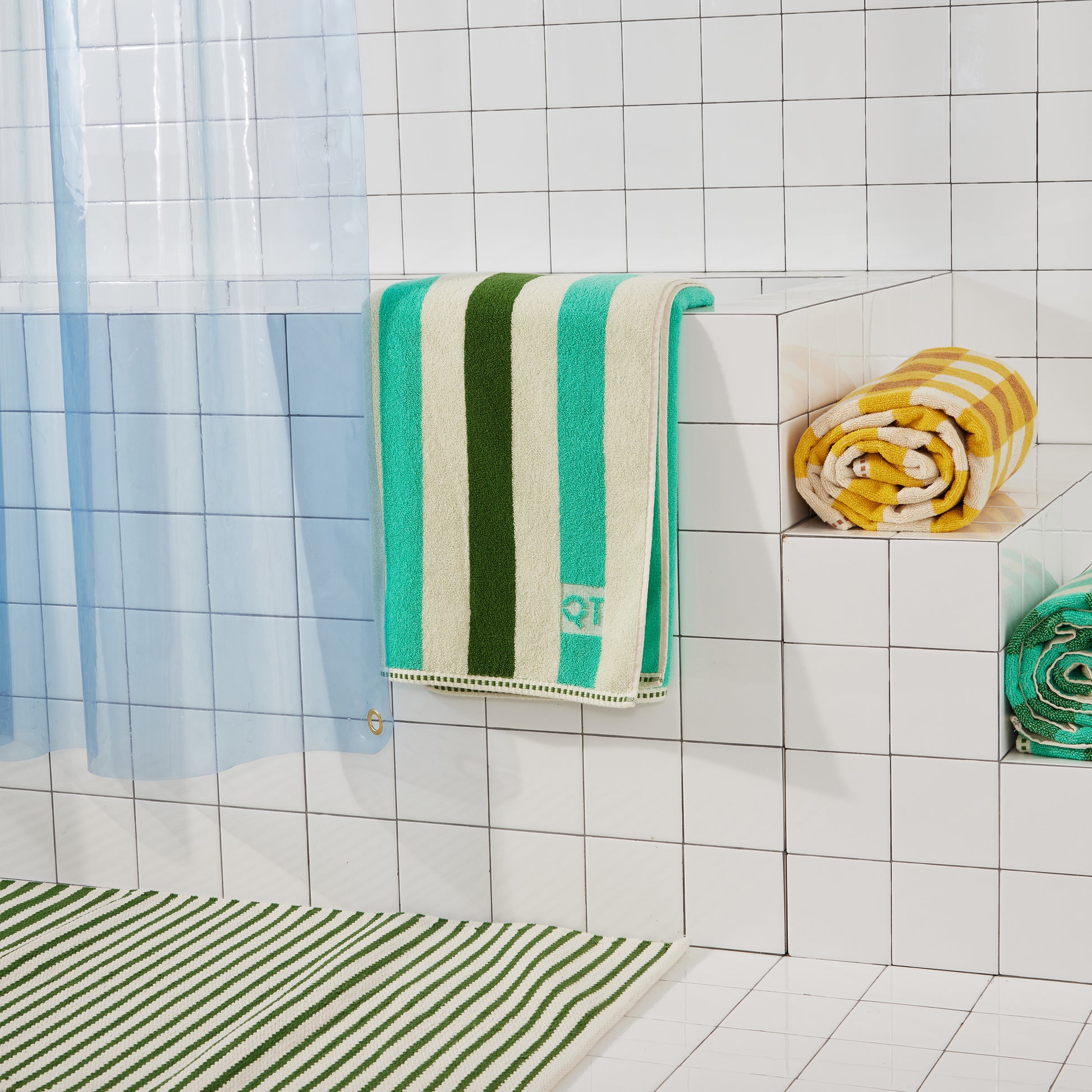 bottom corner of light blue shower cutain with nickel grommet detail and green and yellow towels.