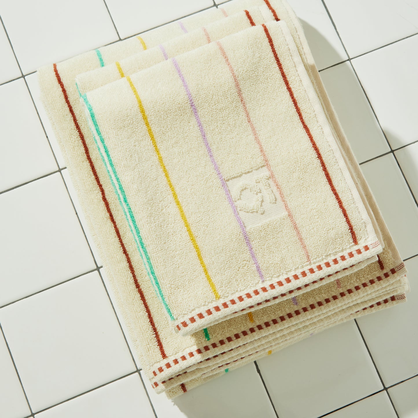 Cream bath and hand towel set with colorful stripes on a tiled floor