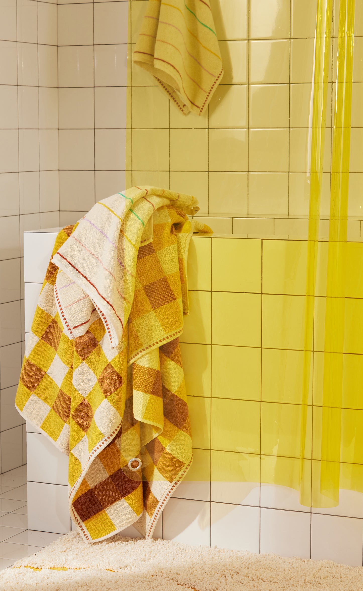 Bottom corner of Sunny Sun Shower with bright yellow EVA and styled with Prism hand towel, Tam Canyon bath sheet and Atlas Canyon bath rug.