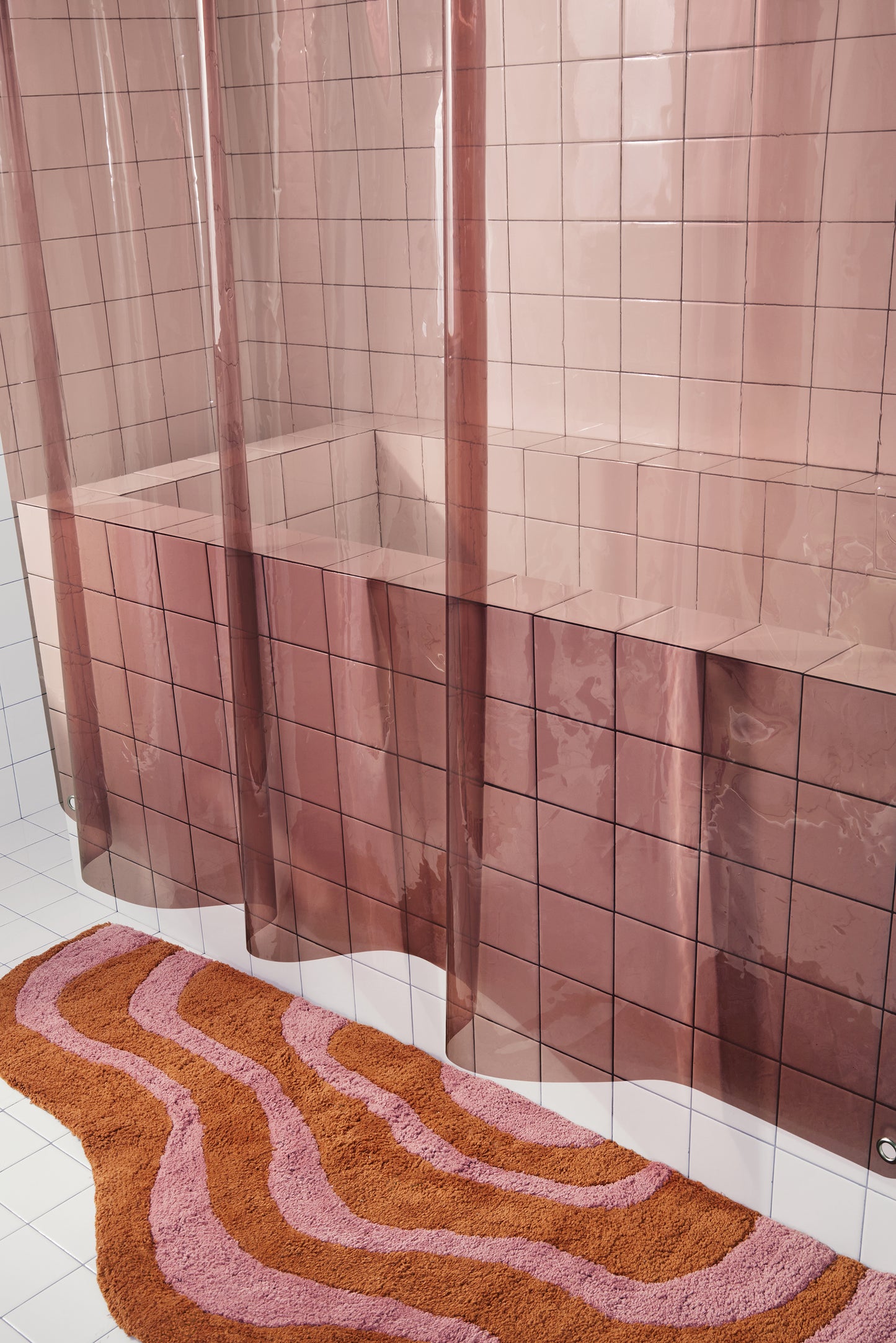 Sun Shower in rose side view of curtain hanging in a white tiled bathroom above pink lost coast rug.