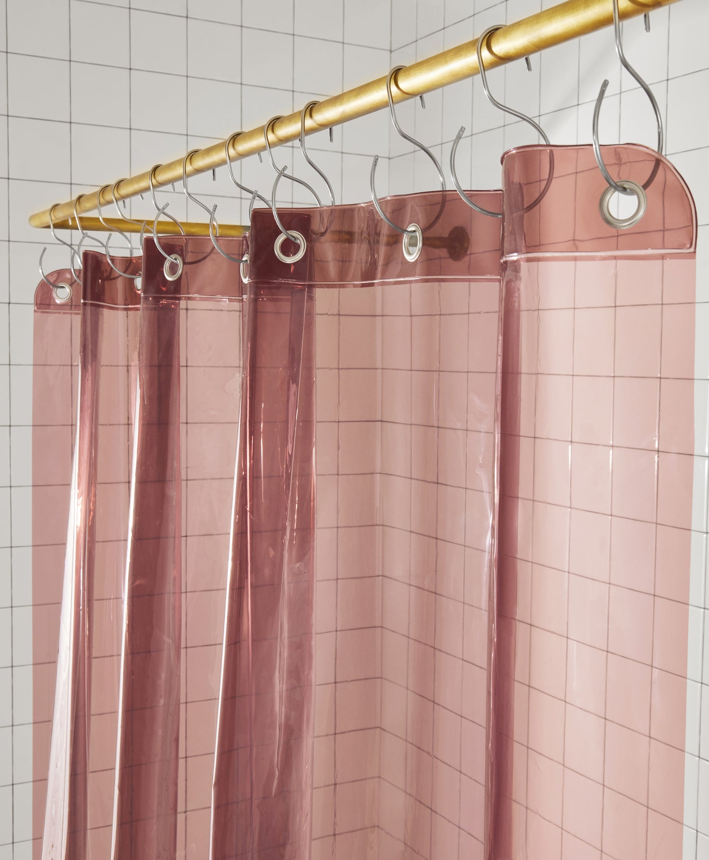 Sun Shower in rose top view of curtain seam hanging from brass rod from silver s hooks in a white tiled bathroom.
