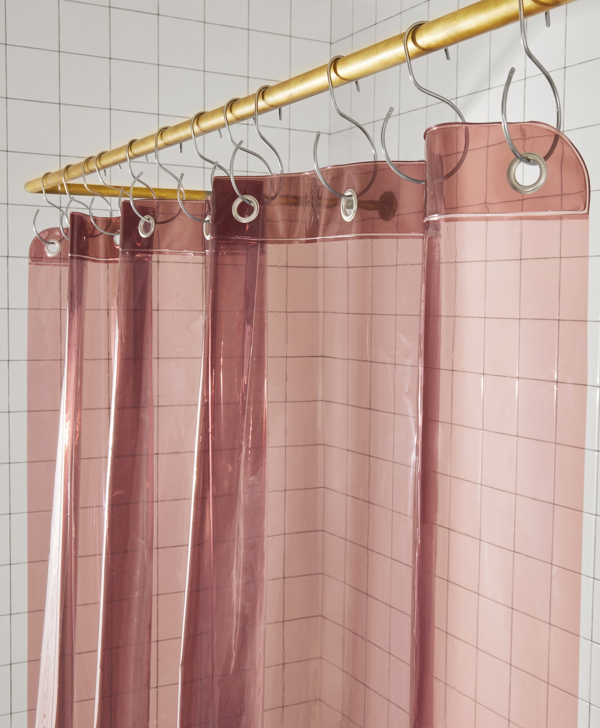Sun Shower in rose top view of curtain seam hanging from brass rod from silver s hooks in a white tiled bathroom.