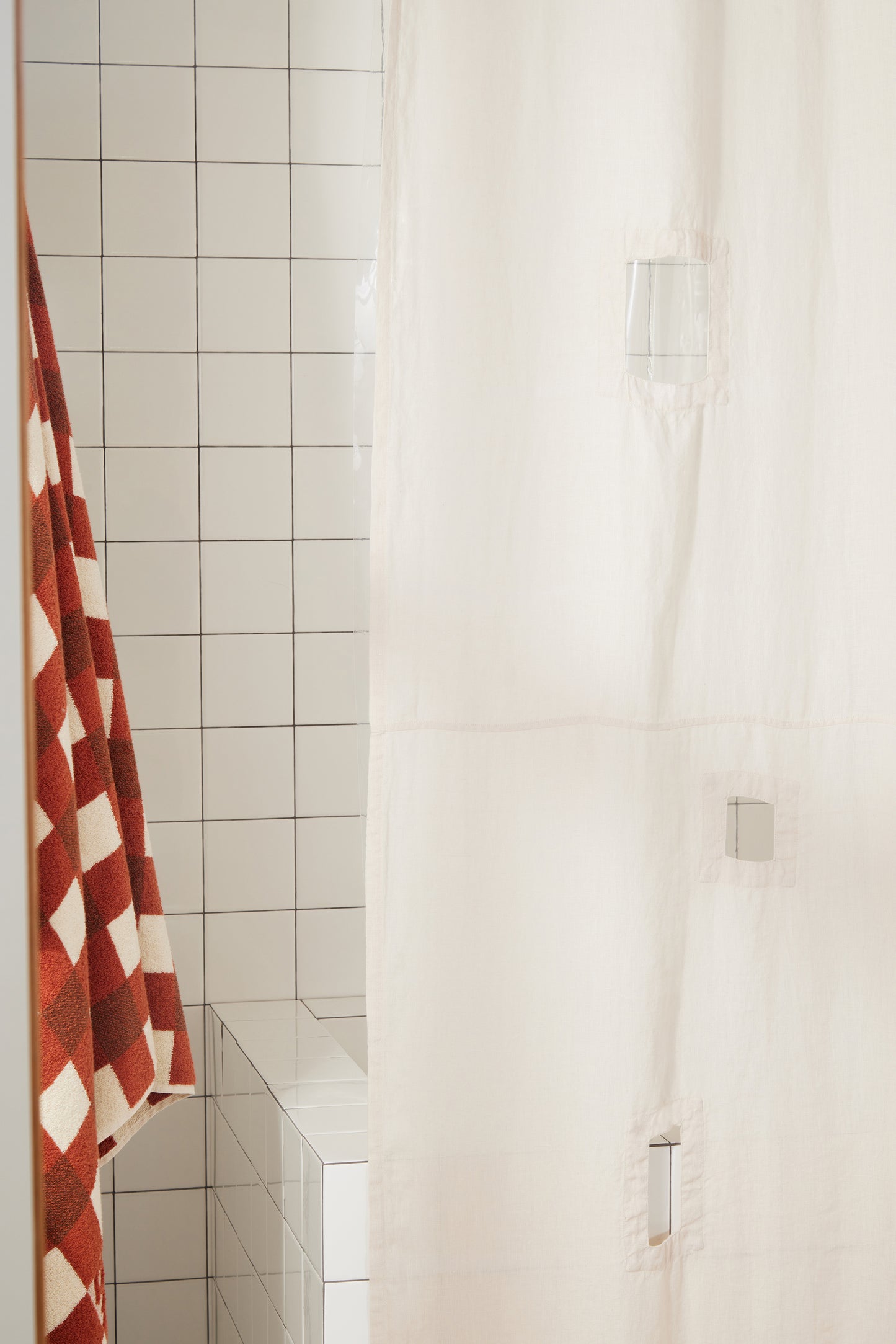 Side view of ronchamp linen shower curtain in sand in white-tiled bathroom.