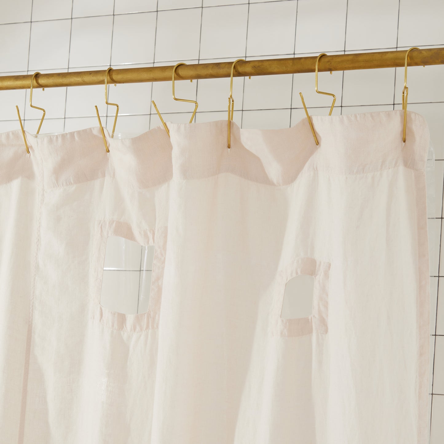 Top seam of ronchamp linen shower curtain in sand hangs on brass rod with brass venice hooks.