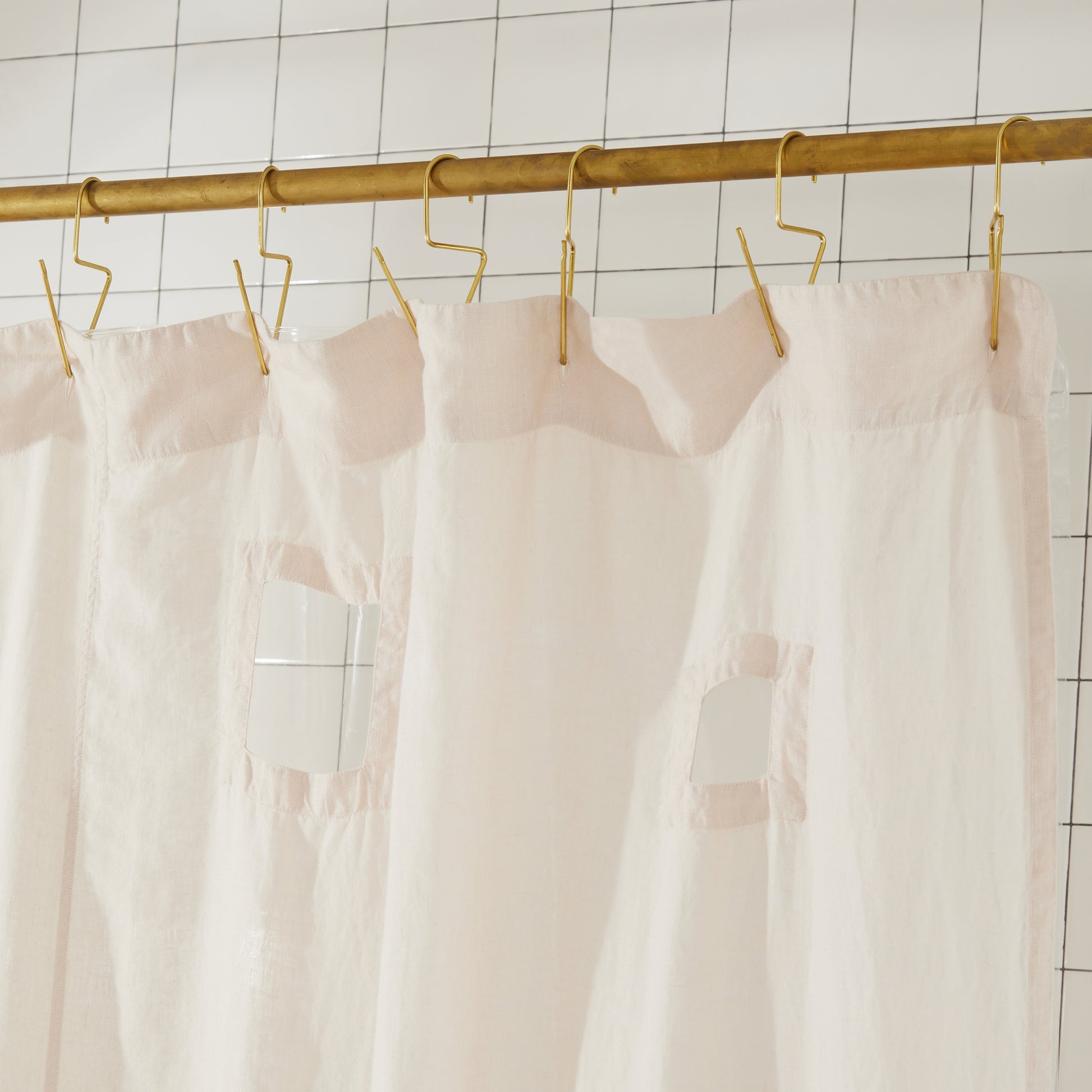 Top seam of ronchamp linen shower curtain in sand hangs on brass rod with brass venice hooks.