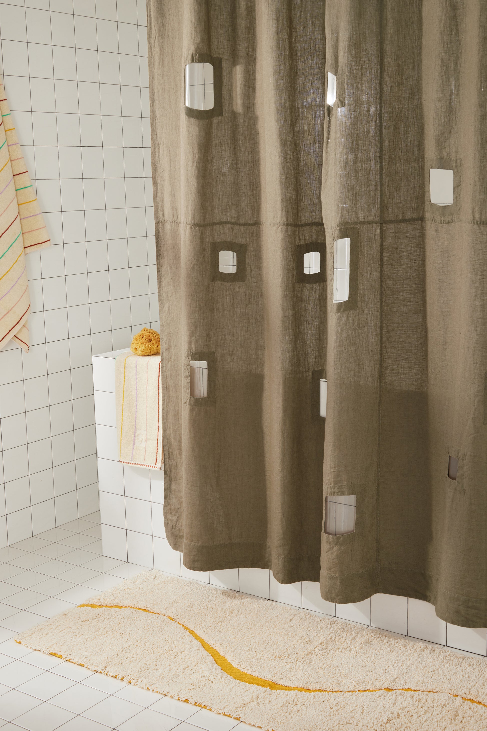 Side detail of ronchamp curtain in olive with rectangular cut outs against white tiled background.