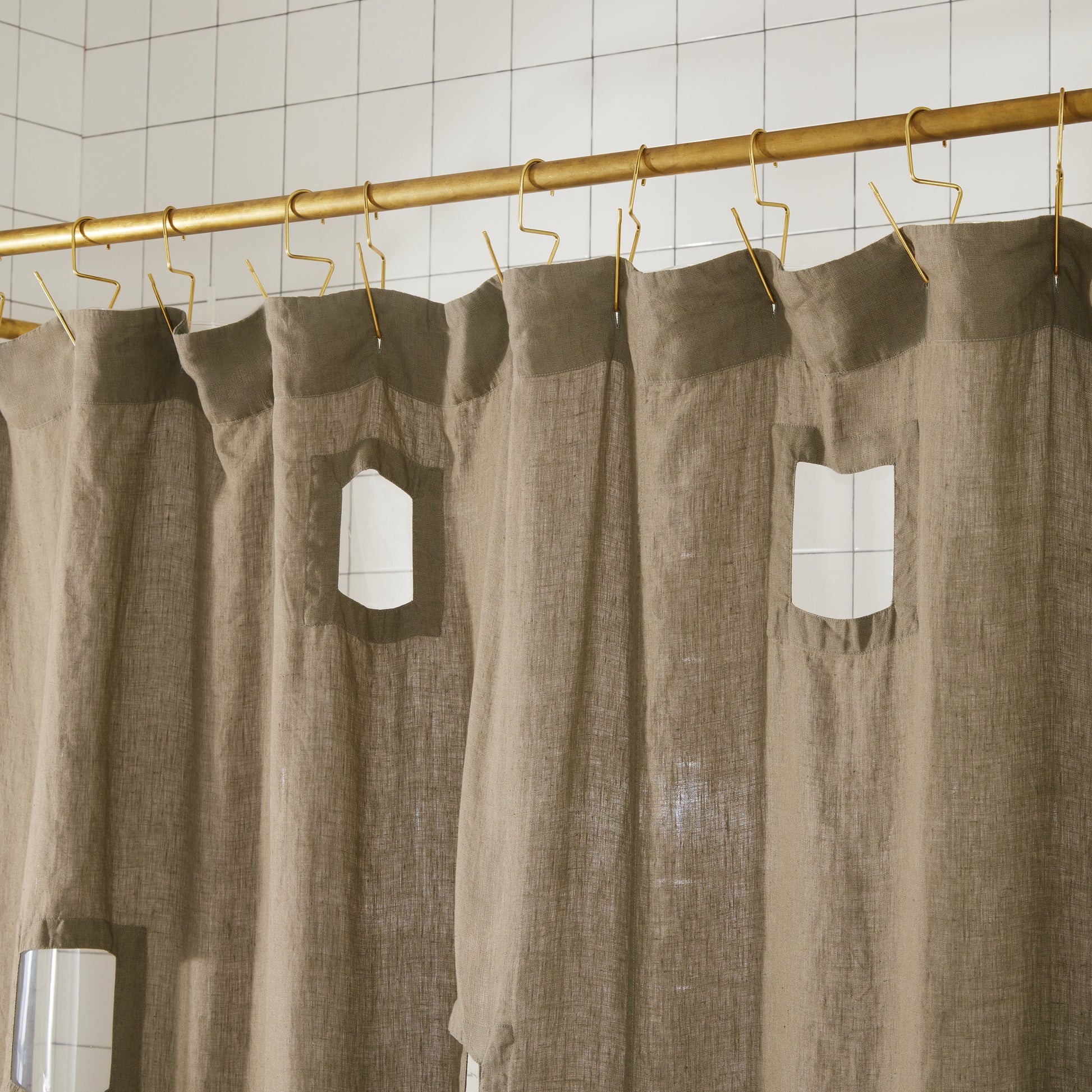 Top seam of Ronchamp linen curtain in olive hanging on brass venice hooks on brass rod.