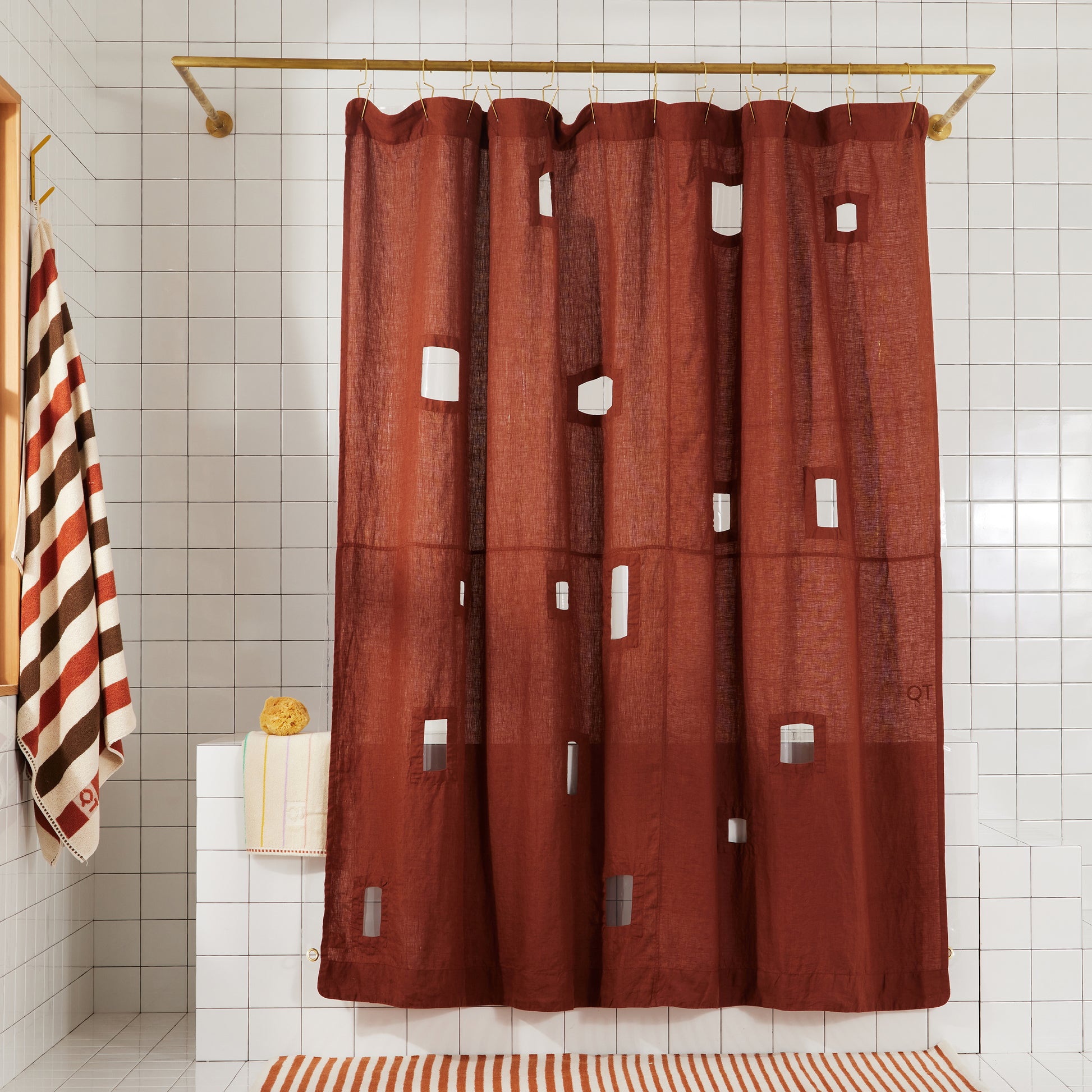 Burgundy linen shower curtain with different sized rectangular window cut-outs hangs in white tiled bathroom.
