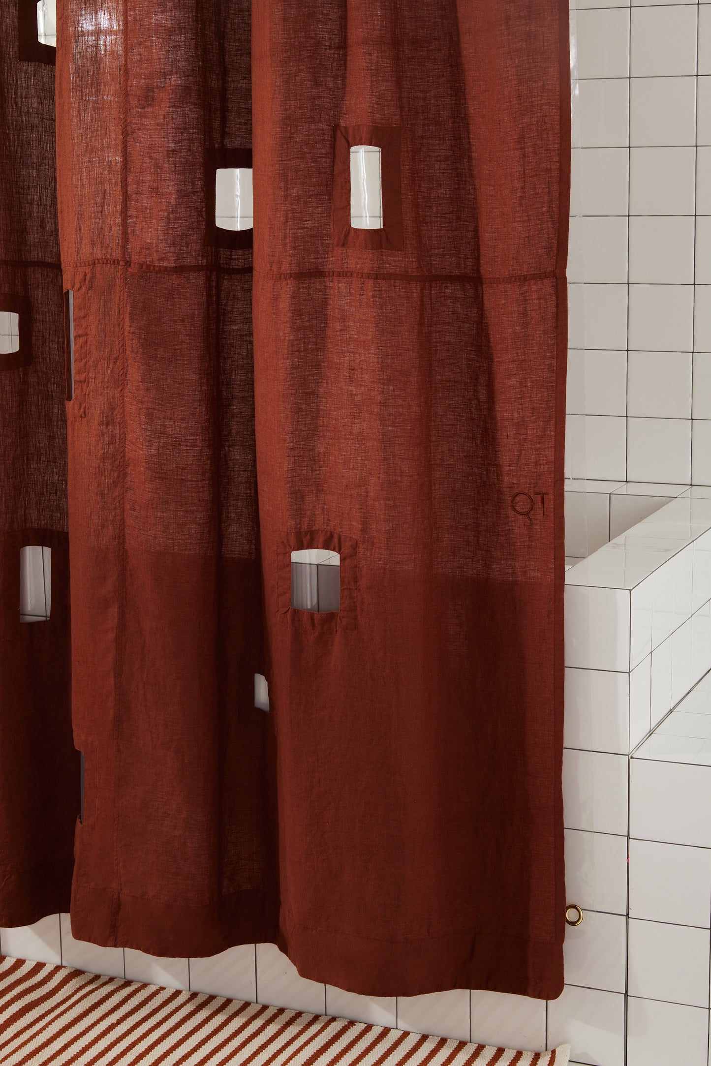 Bottom right corner of burgundy window cut-out shower curtain against white tiled shower.