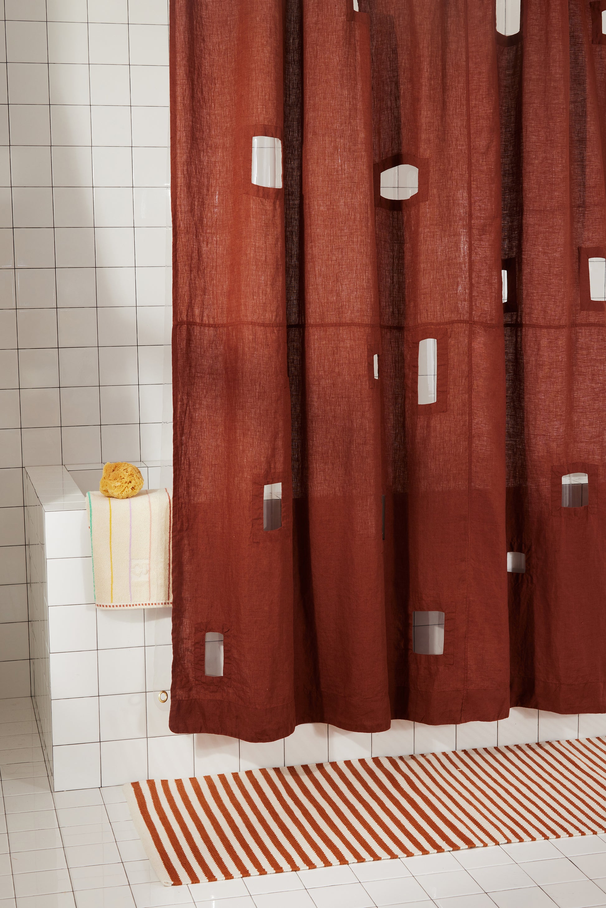 Bottom left corner of burgundy linen shower curtain with transparent cut-out windows against white tiled bathroom.