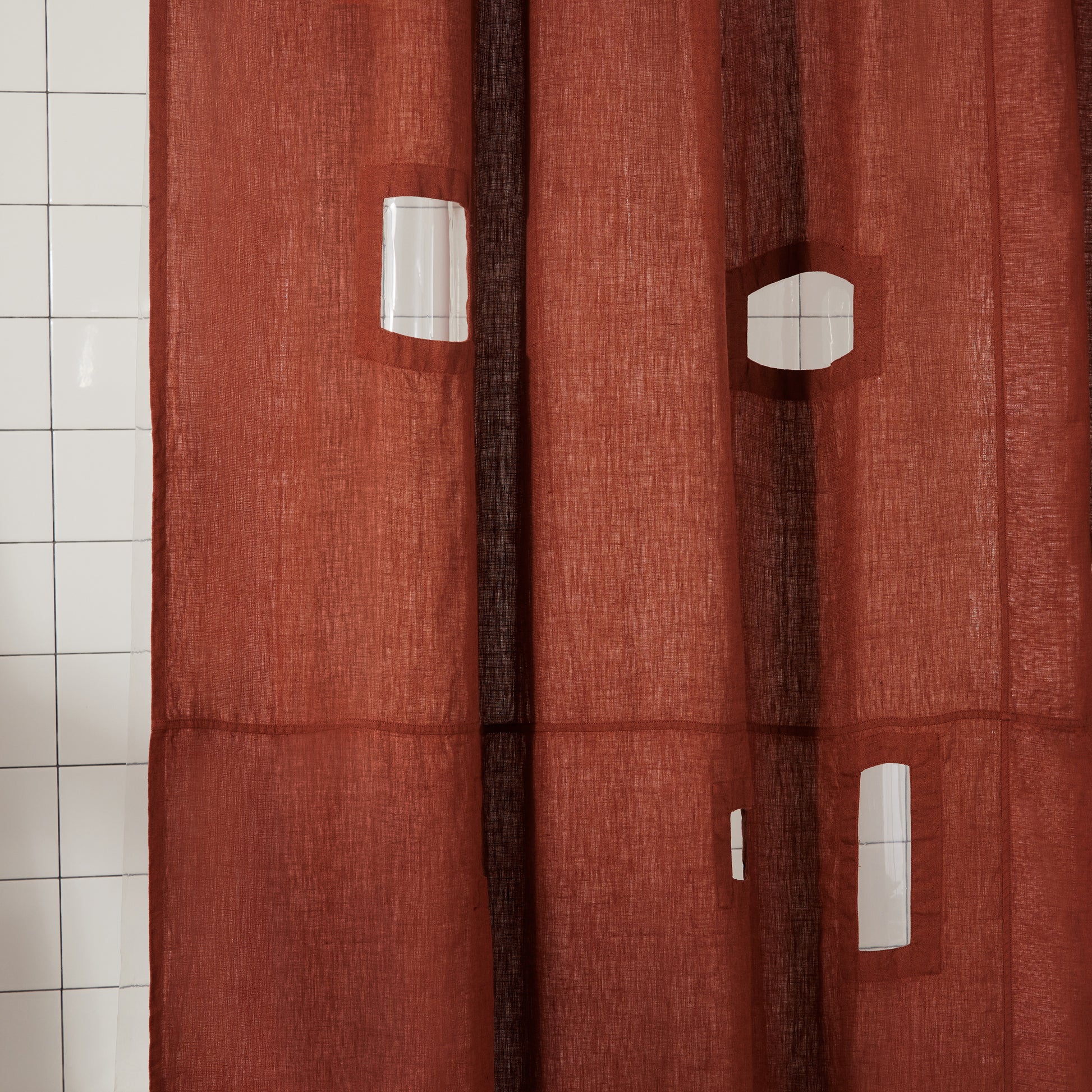 Close up of window cutouts of burgundy linen shower curtain showing white tiled backdrop.
