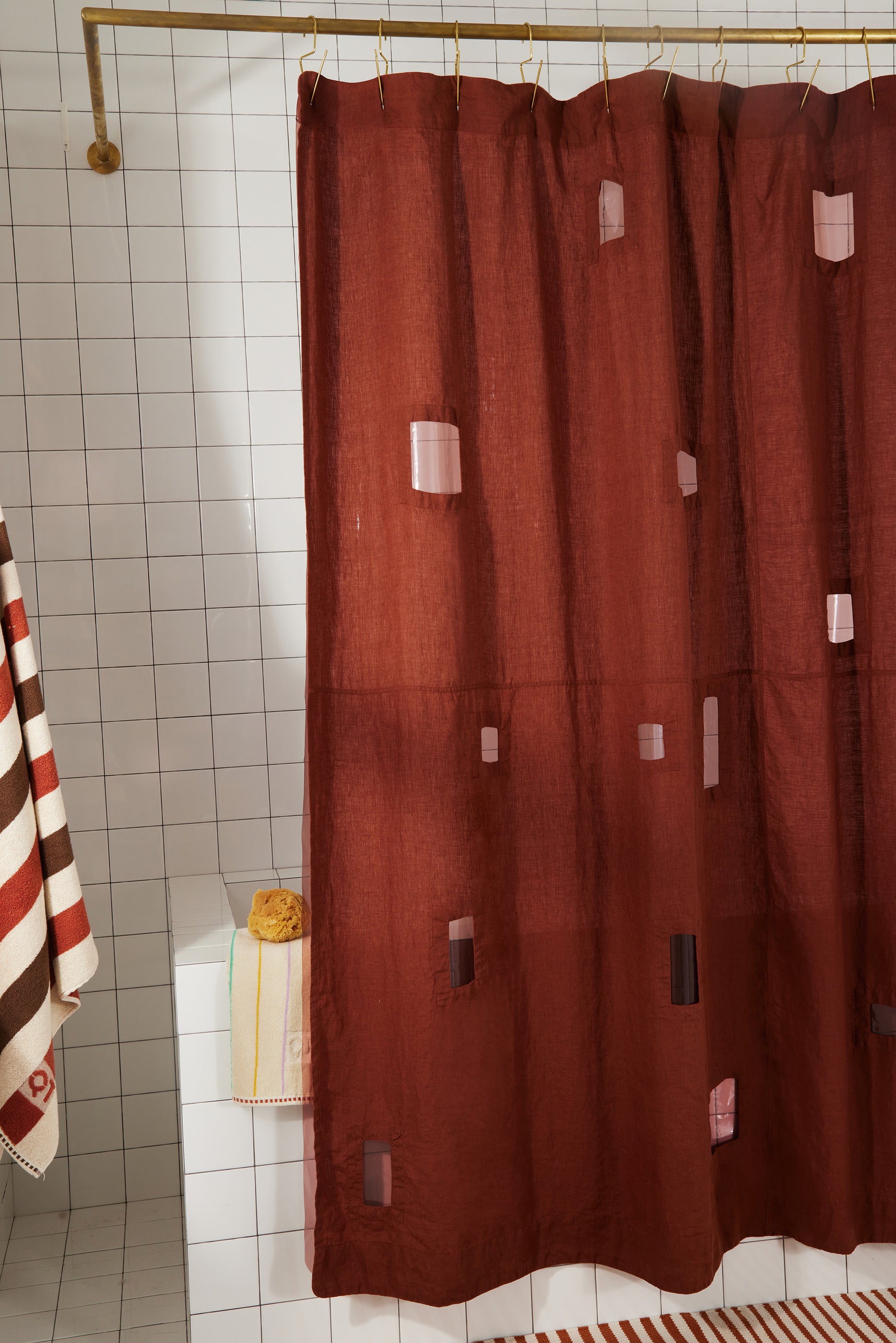 Burgundy linen shower curtain with assorted rectangular window cutouts hanging in styled bathroom.