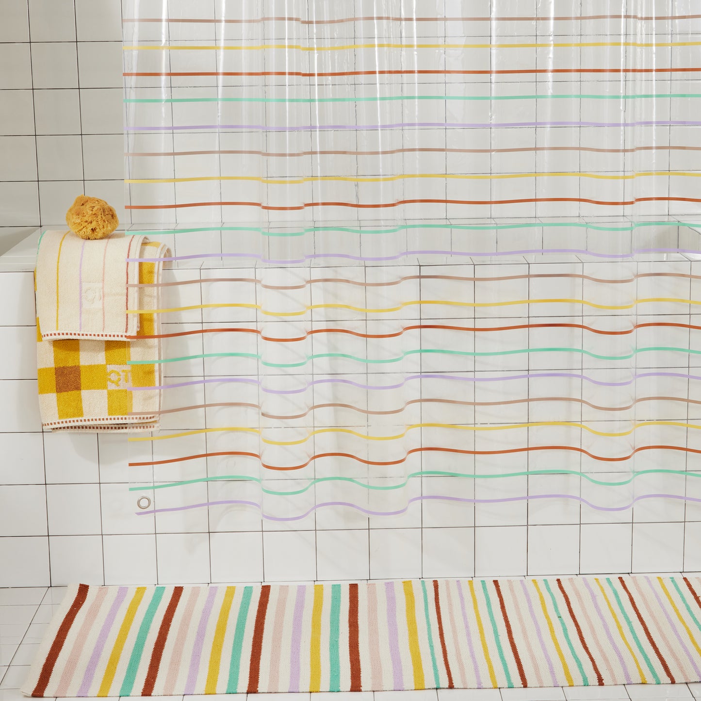 Bottom half of shower curtain with silver grommet on bottom corner and multi-color pinstripes going horizontal. Stripes are green, lavender, rose, yellow and clay.