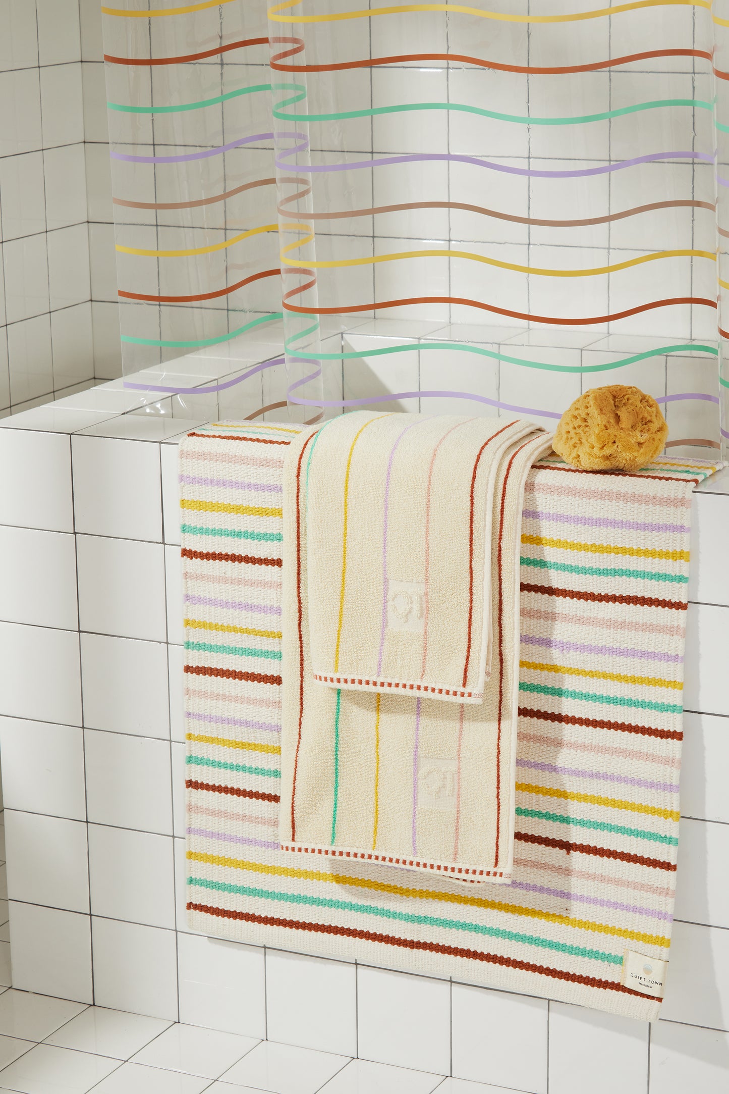 Multi colored striped prism rug and prism towels are styled over a white tiled bathroom tub with the prism sunshower curtain.