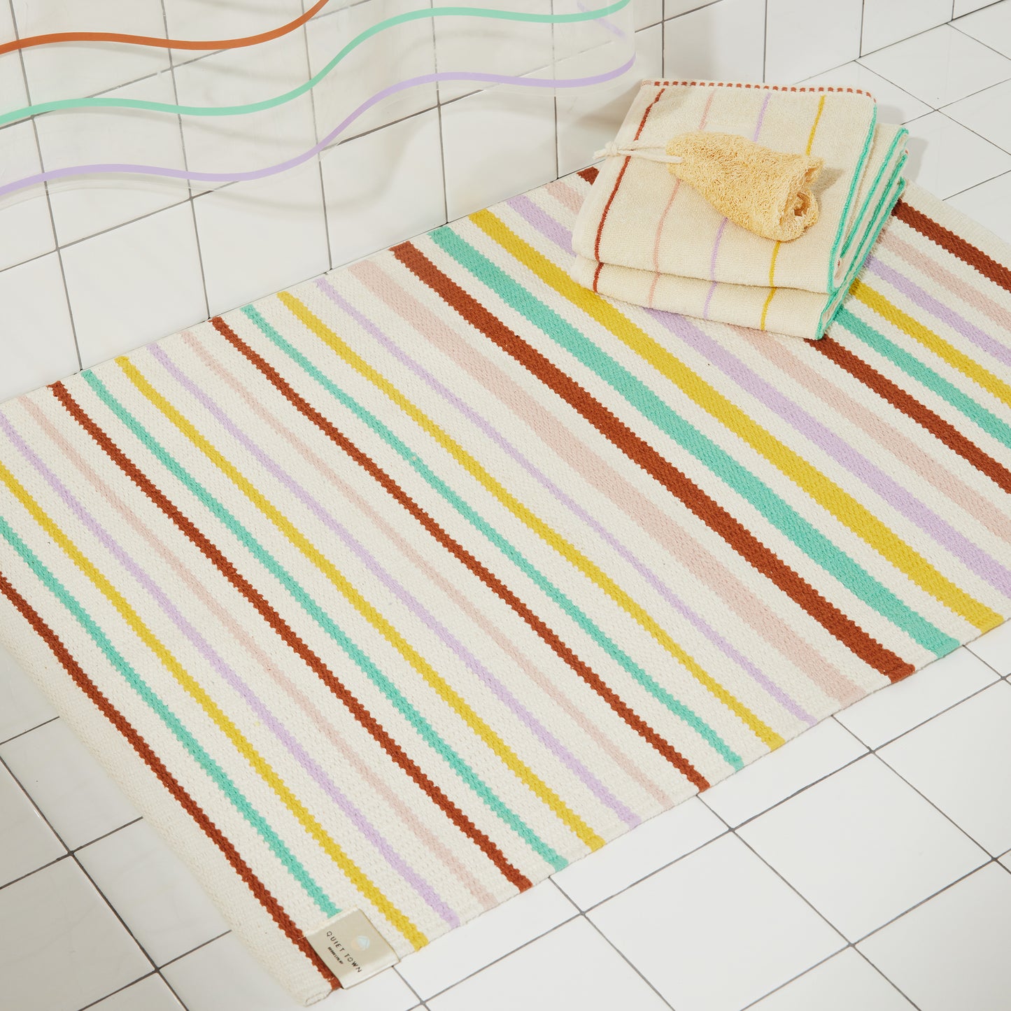 Multi colored striped prism rug and prism towels are styled laying flat on a bathroom floor with the prism sun shower curtain.