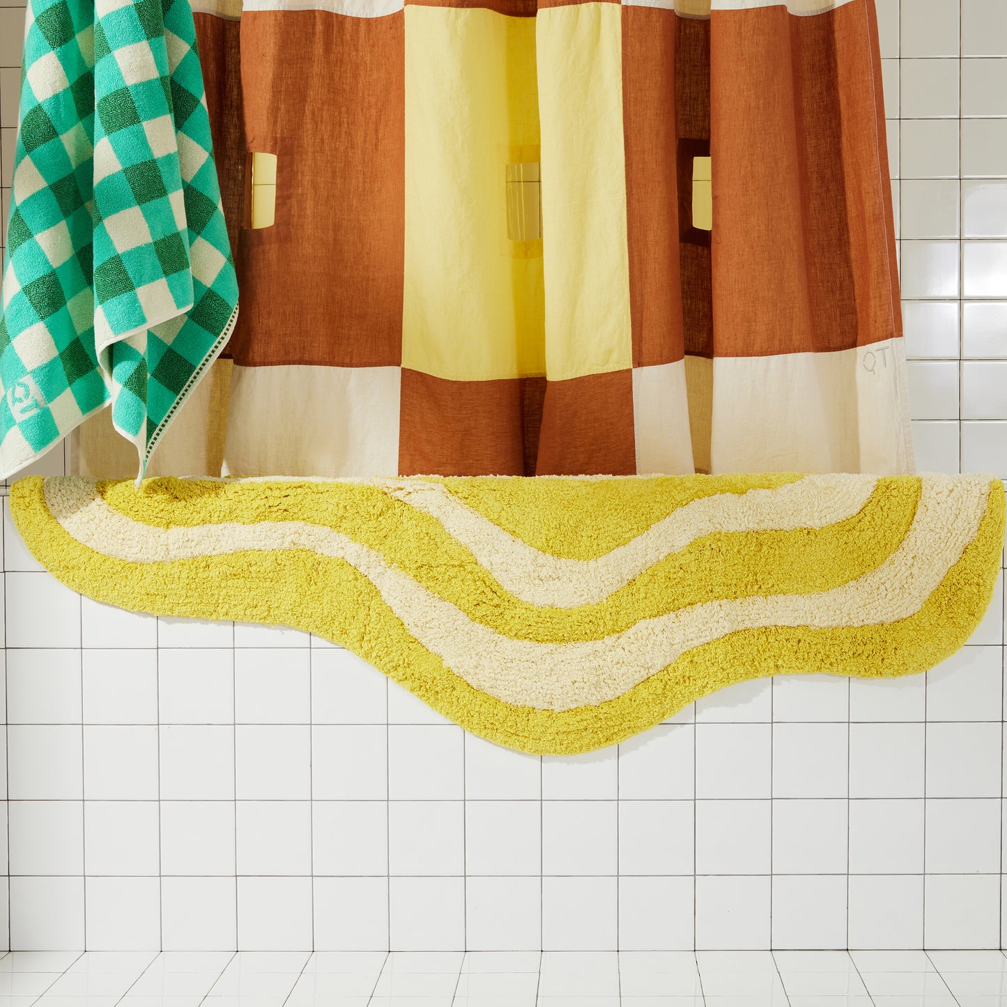 Yellow and cream wavy bath runner laying over white tiled bath tub with clay and cream linen curtain and green checker towel.