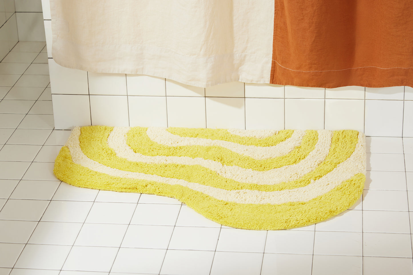 Yellow and cream wavy bath rug laying flat on white bathroom tile.