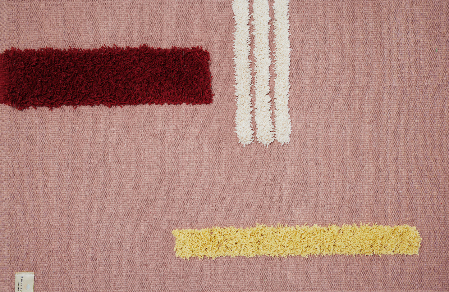 Close up of rose colored reyes rug with 3 white stripes, one burgundy and one yellow stripe.