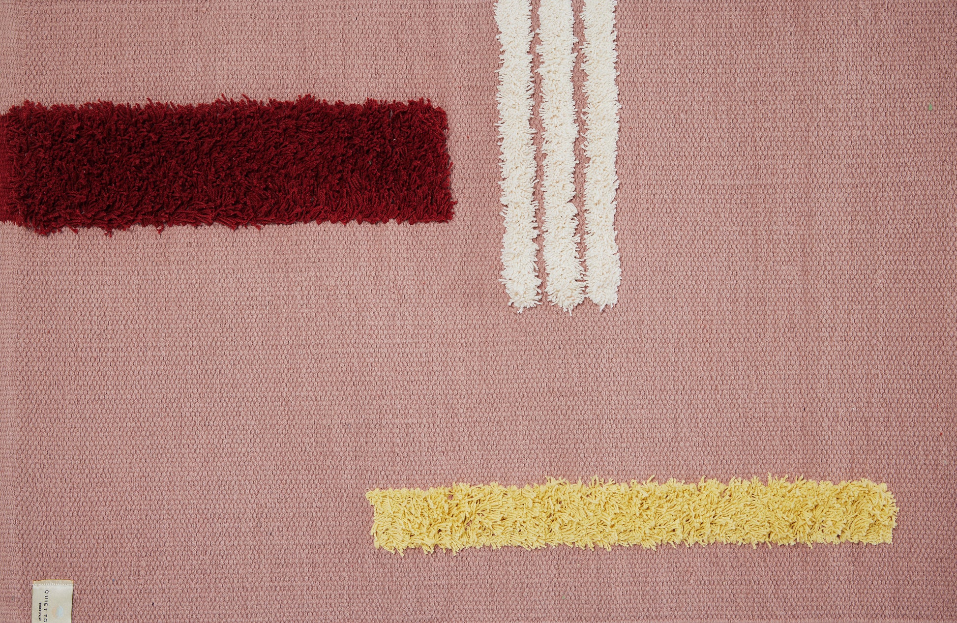 Close up of rose colored reyes rug with 3 white stripes, one burgundy and one yellow stripe.