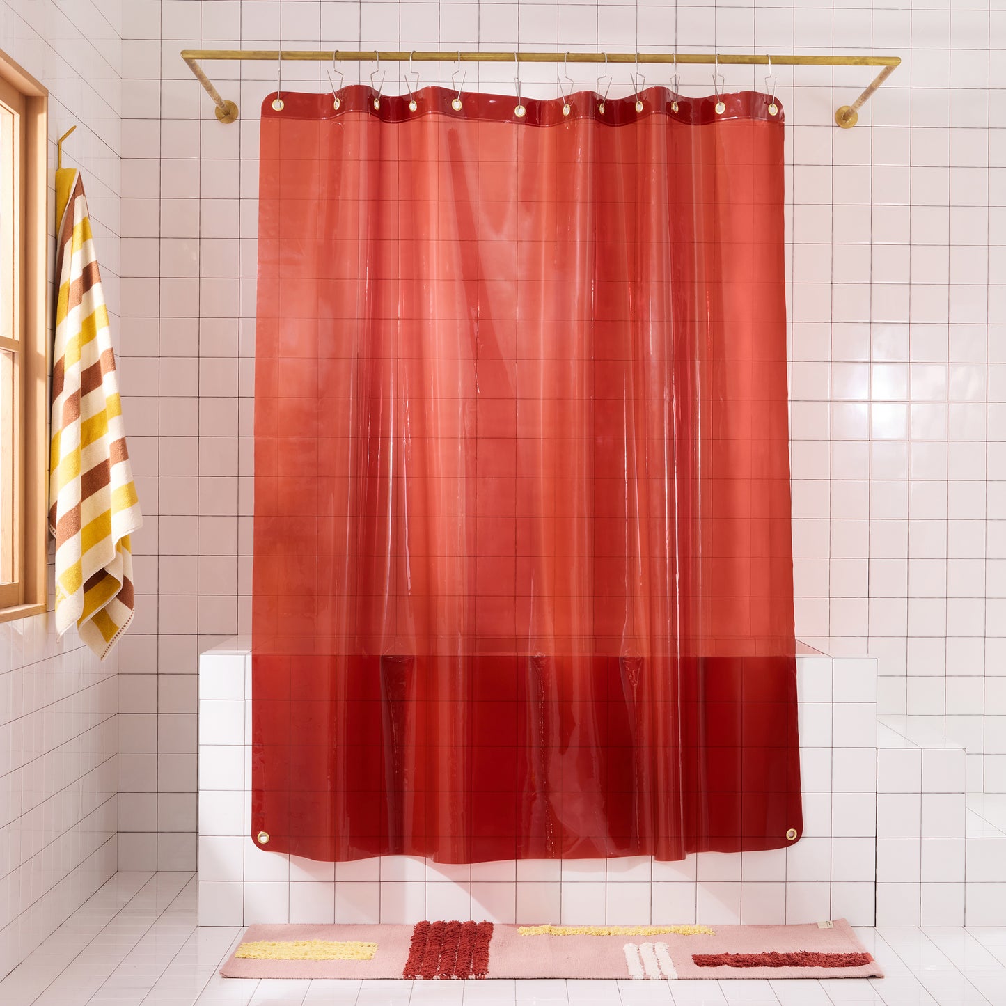 Sun shower curtain in brick hanging over bathtub styled in a white tiled bathroom with rose reyes rug and catalina bath sheet in canyon.