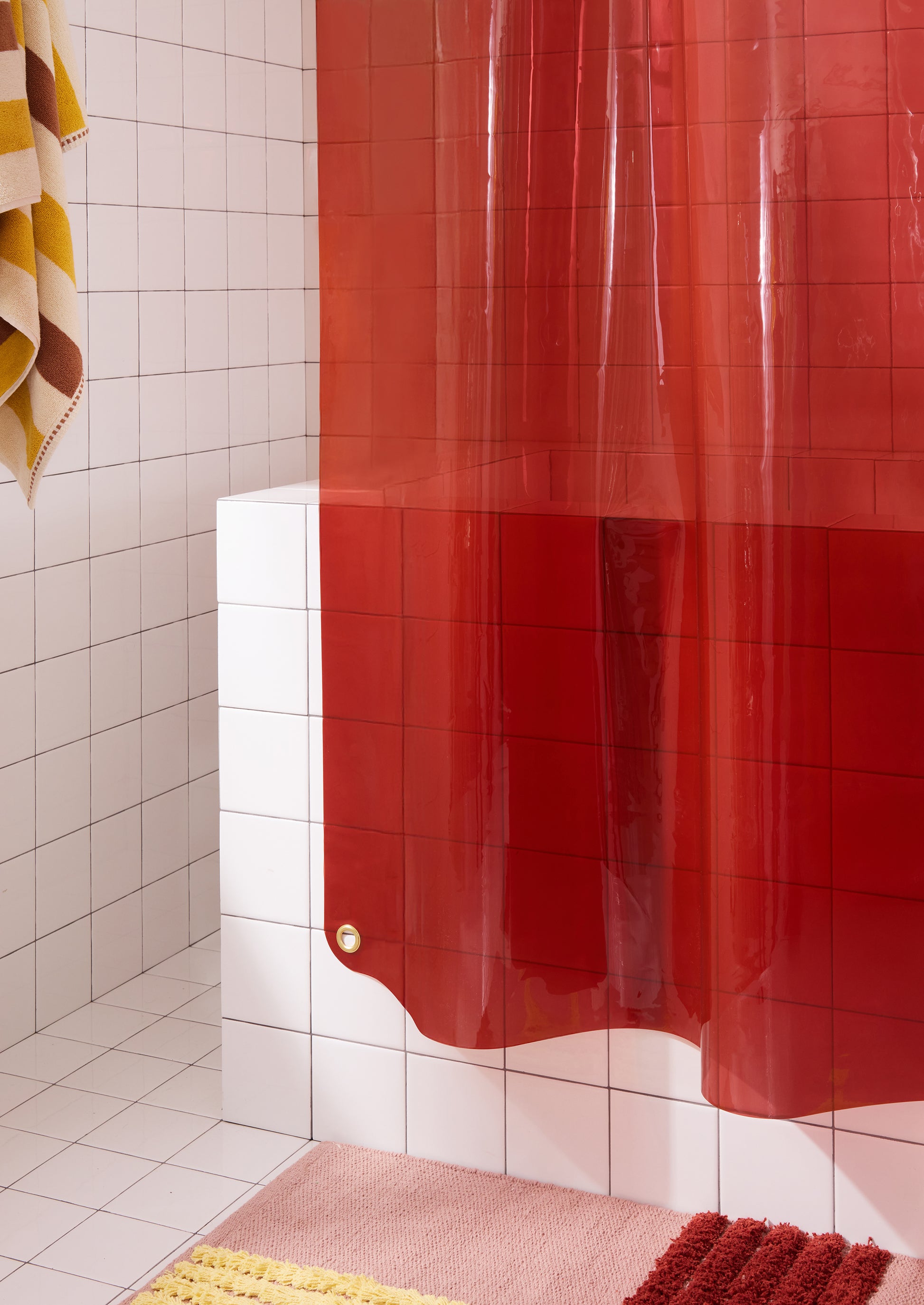 Bottom left corner of Sun Shower brick curtain hanging in white tile bathroom.