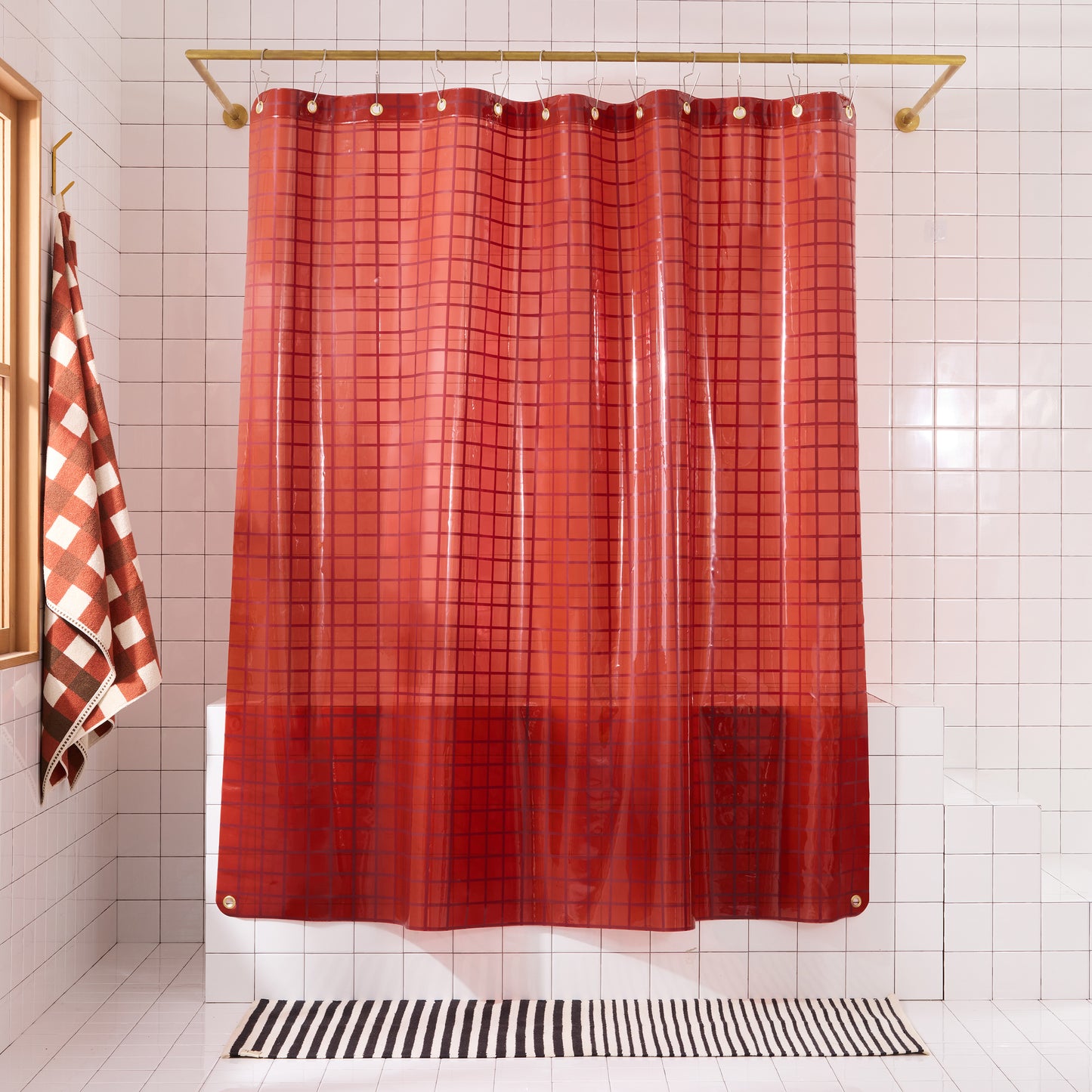 Brick red 2x2 grid sun shower curtain hanging against white tiled bathroom.