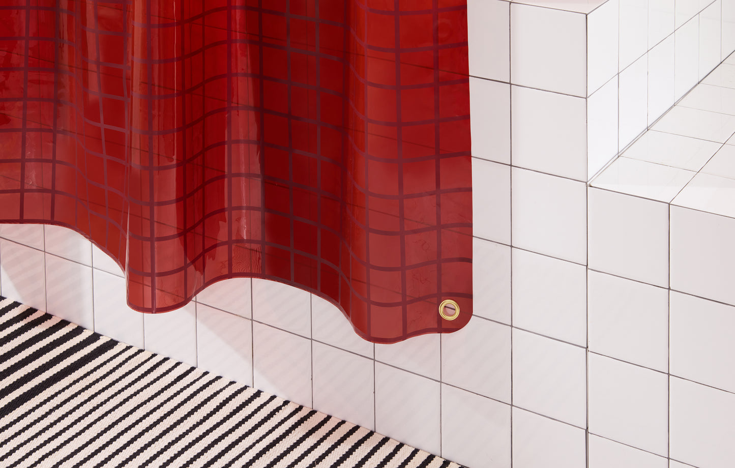 Bottom right corner of 2x2 grid sun shower curtain in brick hanging above black and white striped bath mat.
