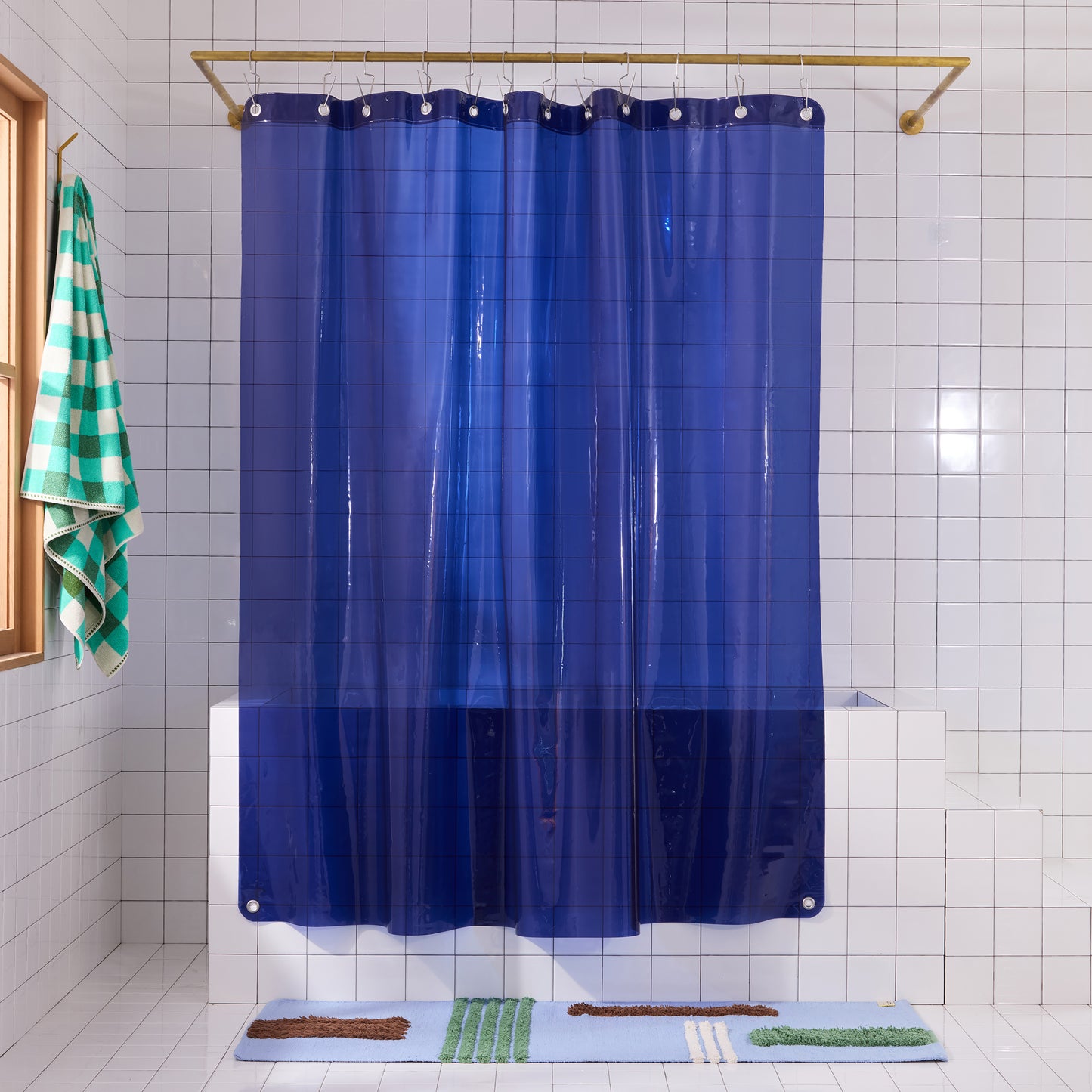 Sun shower curtain in navy hanging over bathtub styled in a white tiled bathroom with reyes atlantic rug and tam bath sheet pine.
