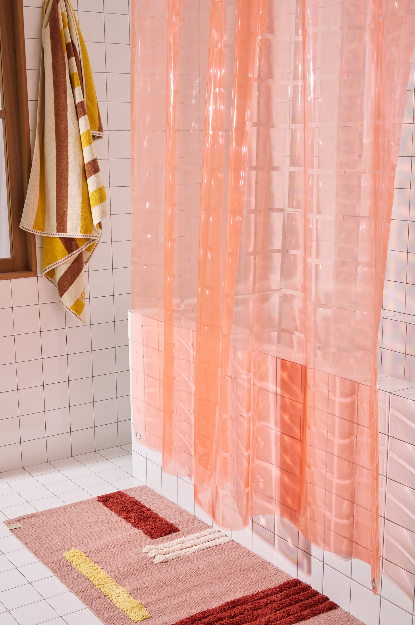 Light pink 3D printed shower curtain hanging in white tiled bathroom with rose colored rug and striped towel.