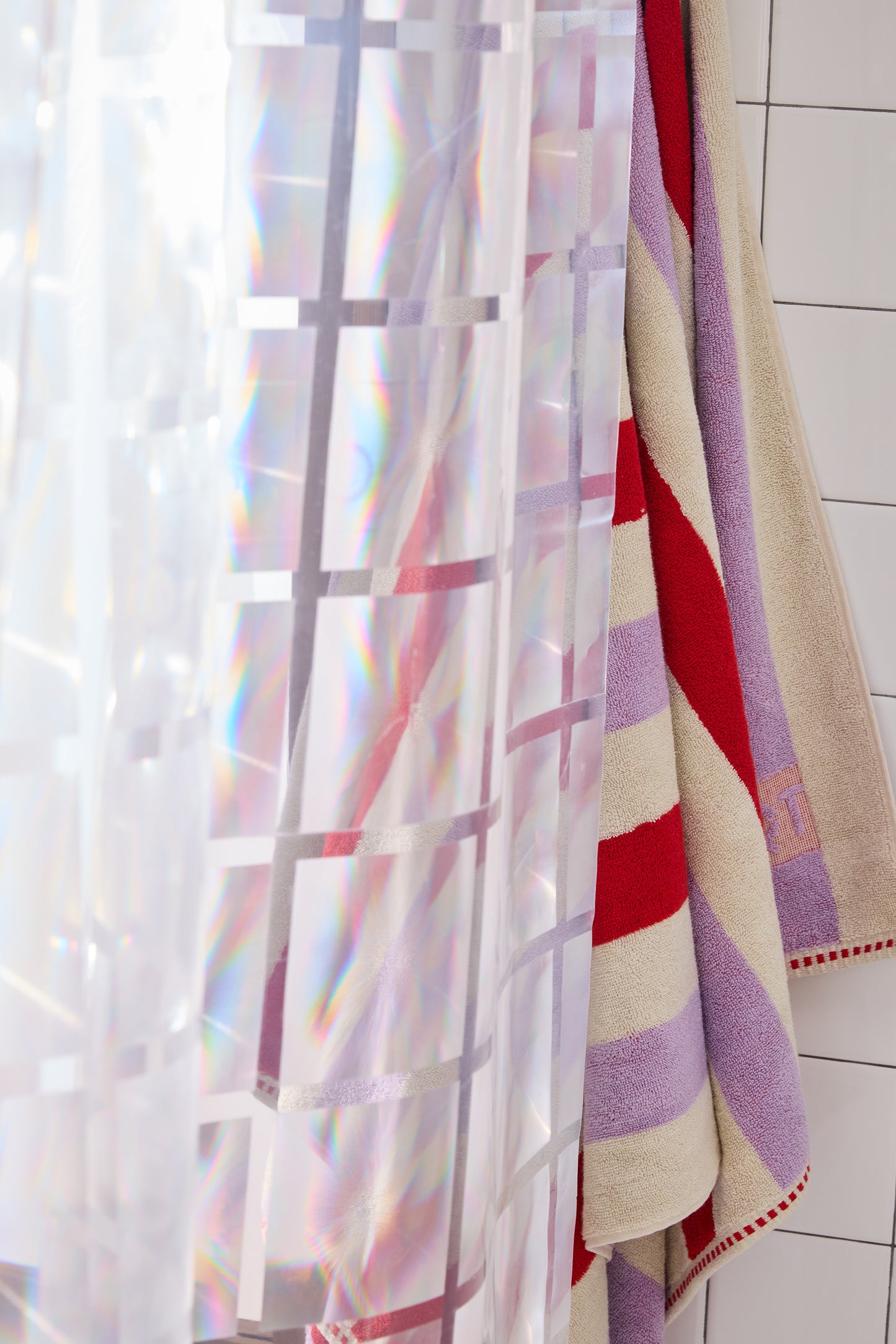 clear 3D curtain hanging in bathroom with white tile with colorful striped towel.