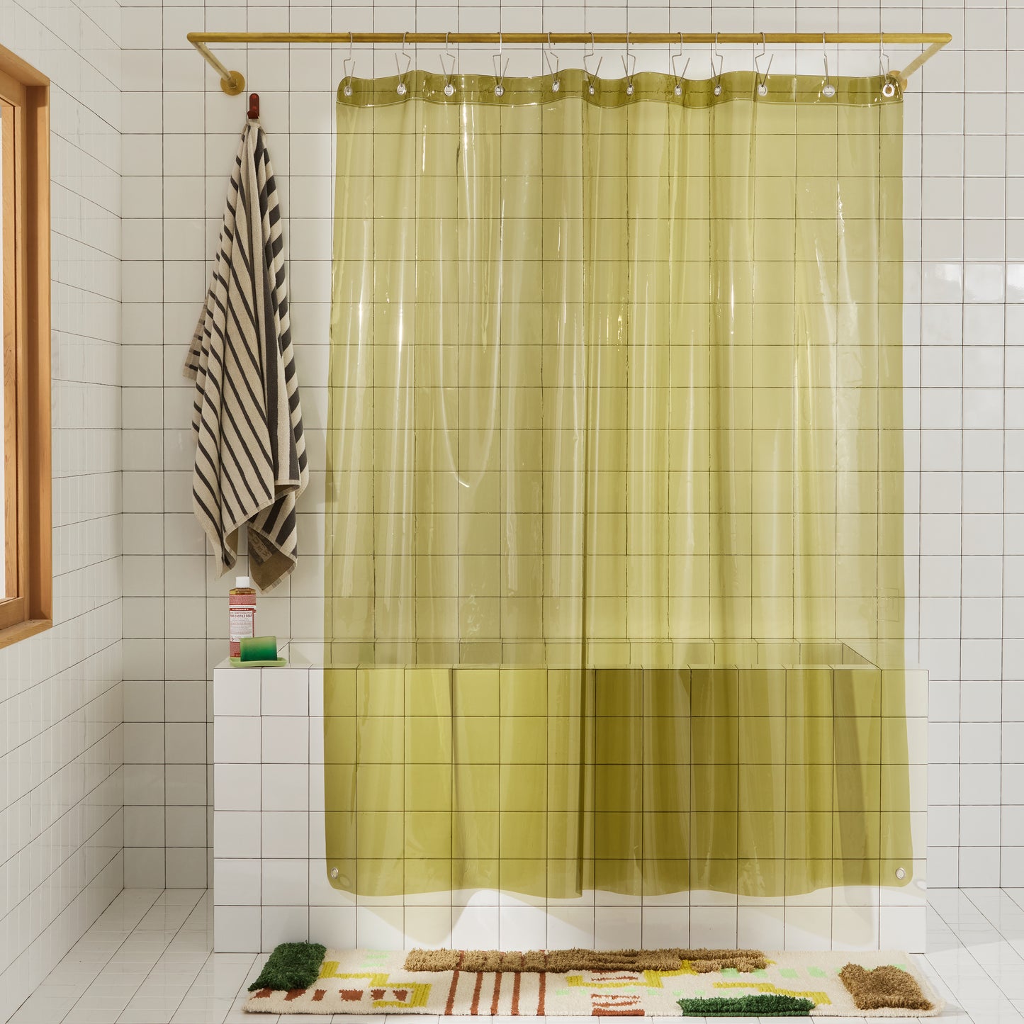 Sun shower curtain in olive hanging over bathtub styled in a white tiled bathroom.