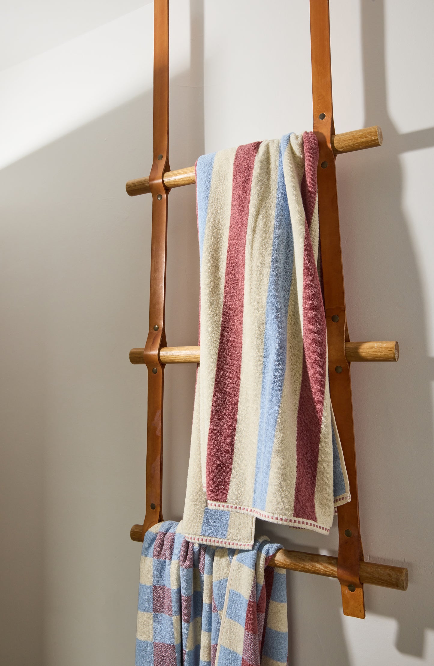 Wooden towel rack with striped and checkered towels against a white wall