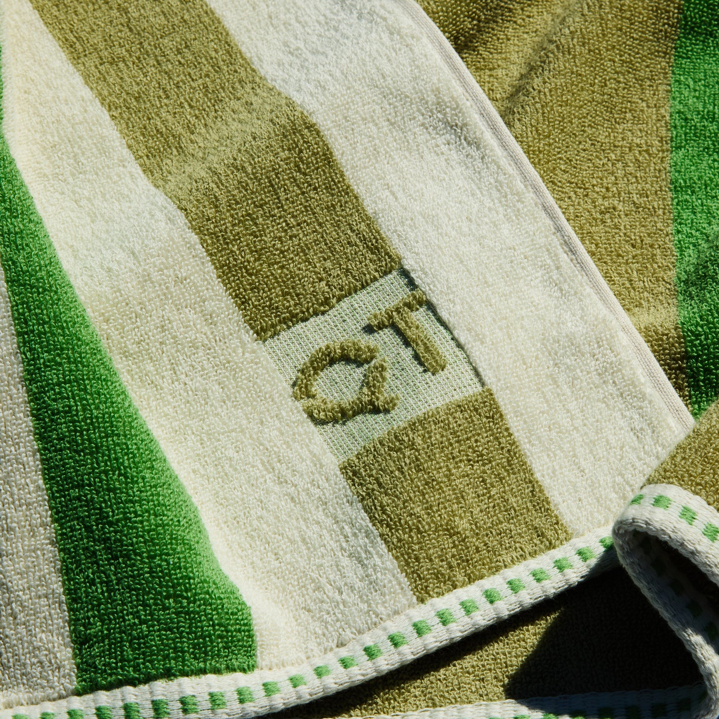 Close-up of a green and beige striped towel with 'QT branding.