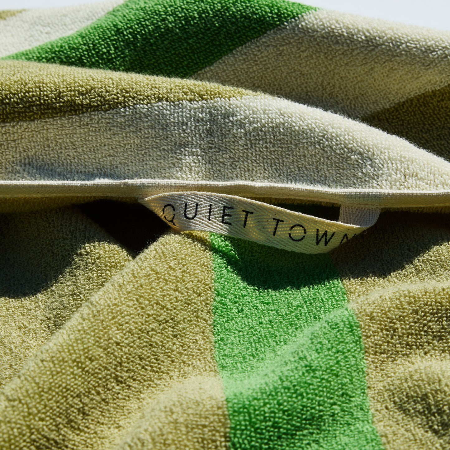 Close-up of a green and cream striped towel with a 'QUIET TOWN' hanging loop.