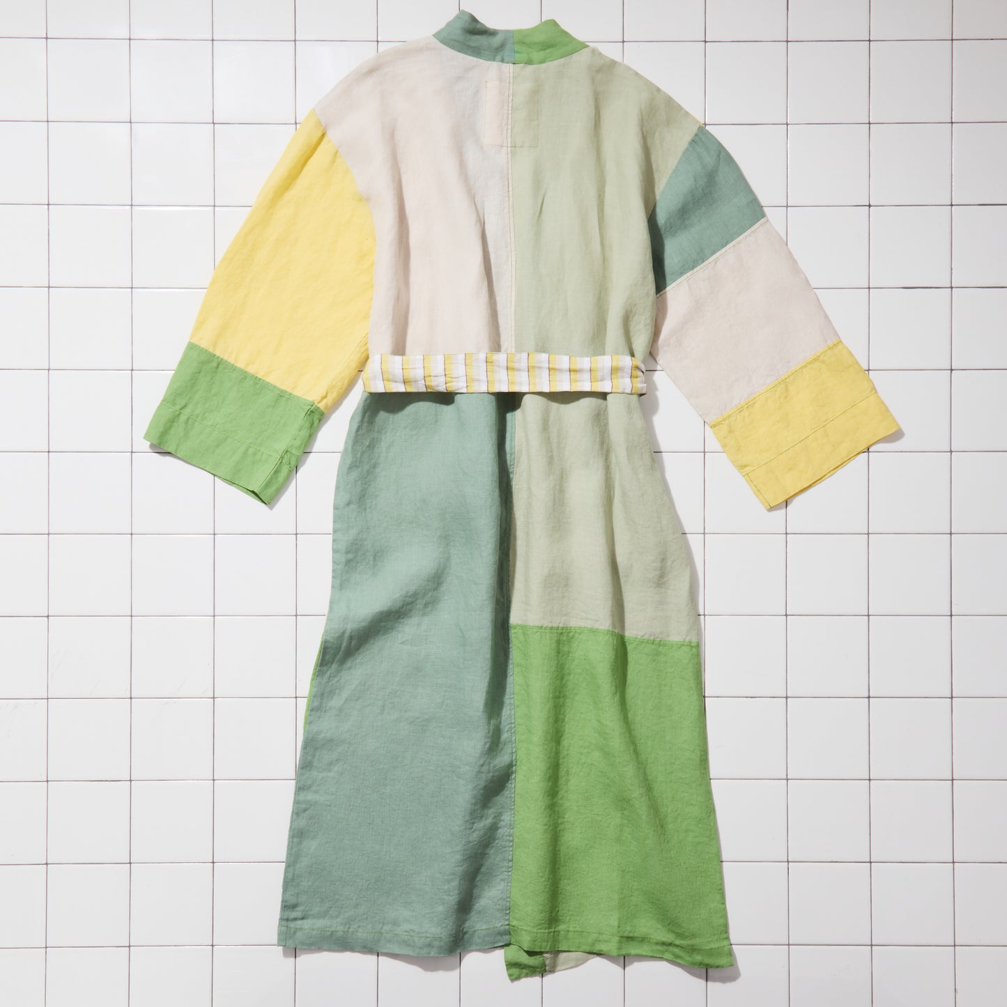 Green and yellow linen bathrobe on white tiled floor.