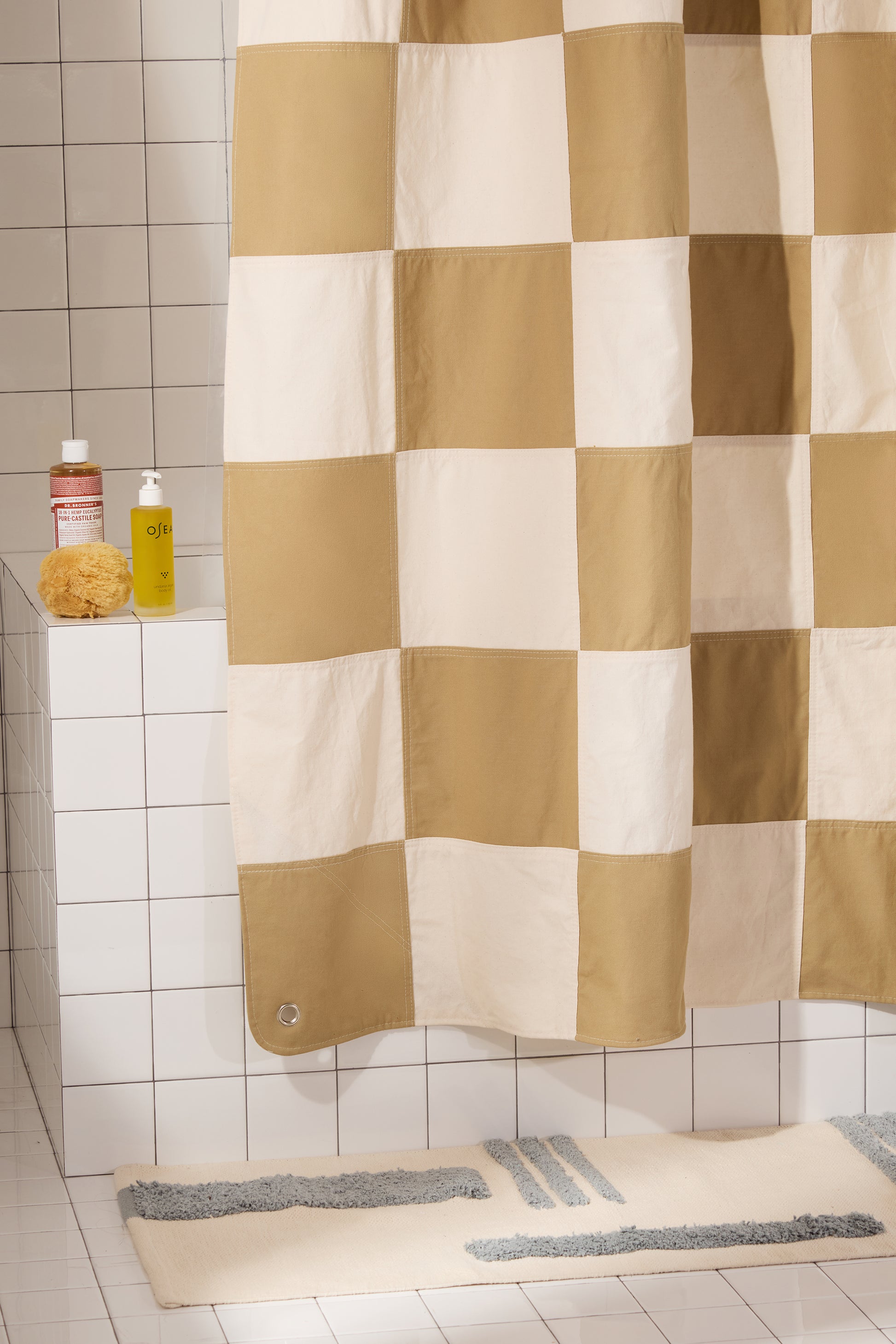 Checkered shower curtain in a bathroom with bath mats and bottles on a ledge.