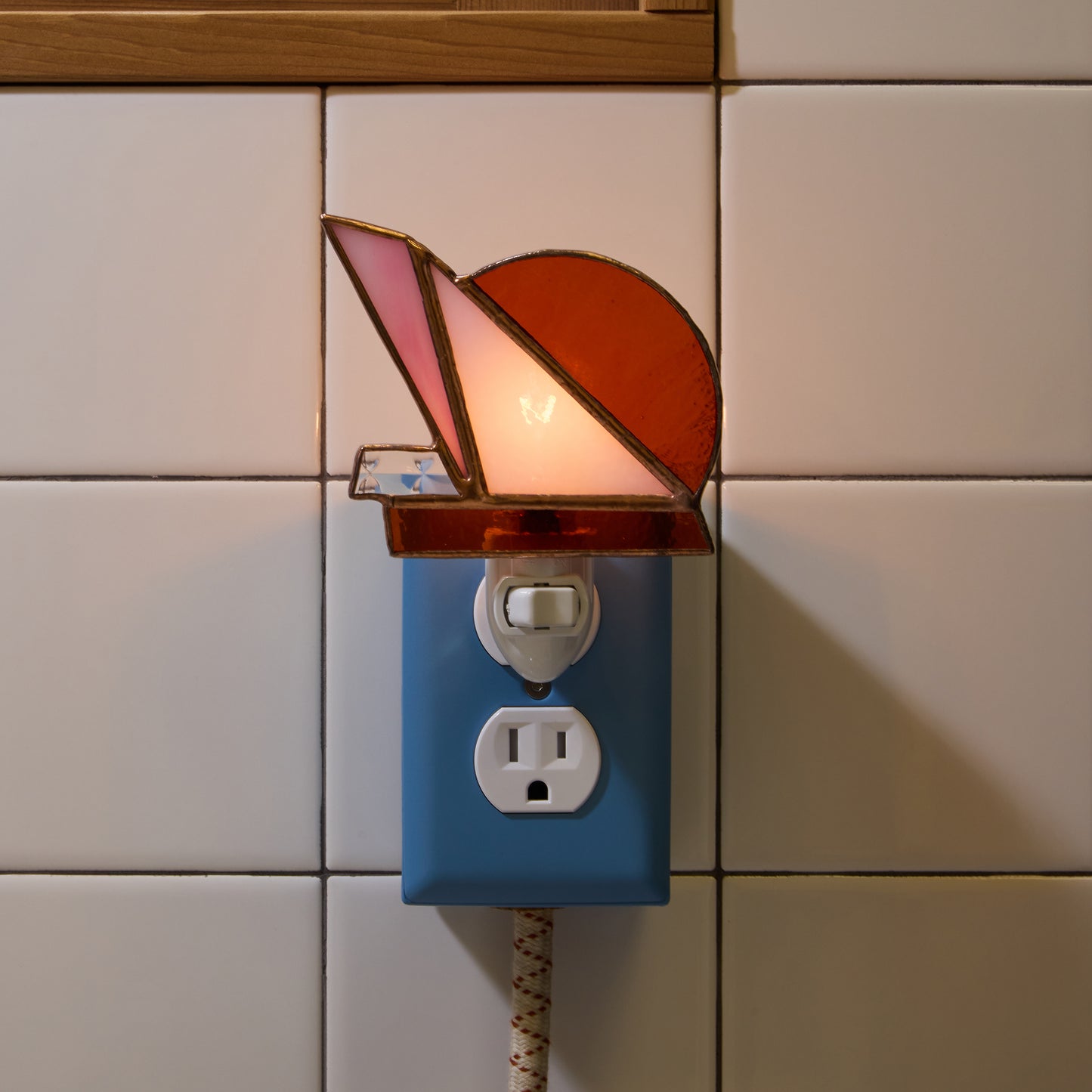 Decorative night light with stained glass design on a tiled wall.