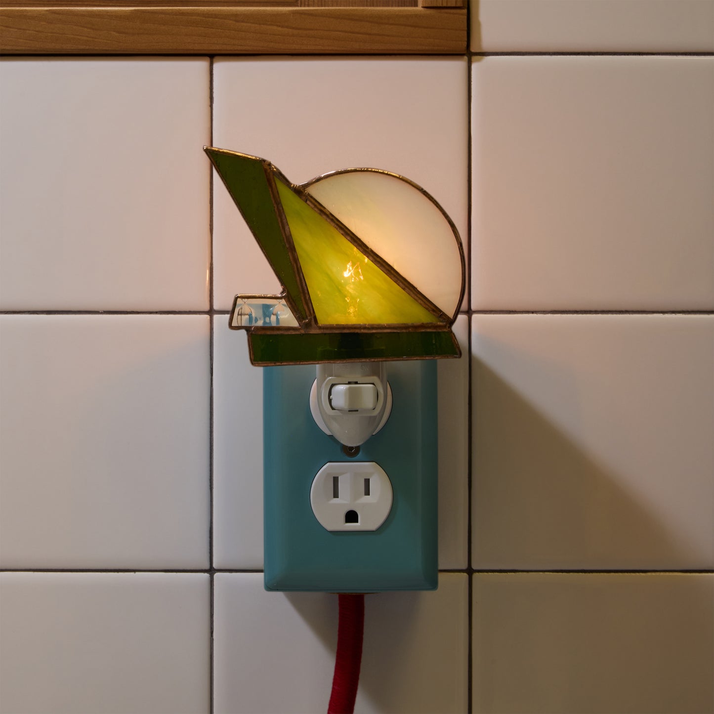 Decorative night light with stained glass design attached to a wall socket with a tiled background