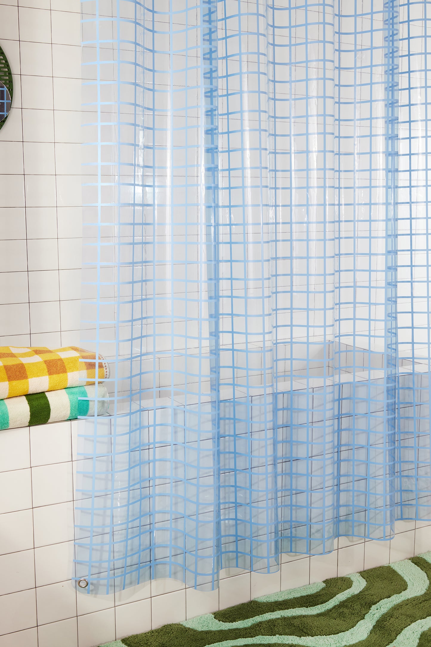 Side view of 2x2 sun shower curtain in atlantic hanging in a white tiled bathroom above the lost coast bath mat in grass.