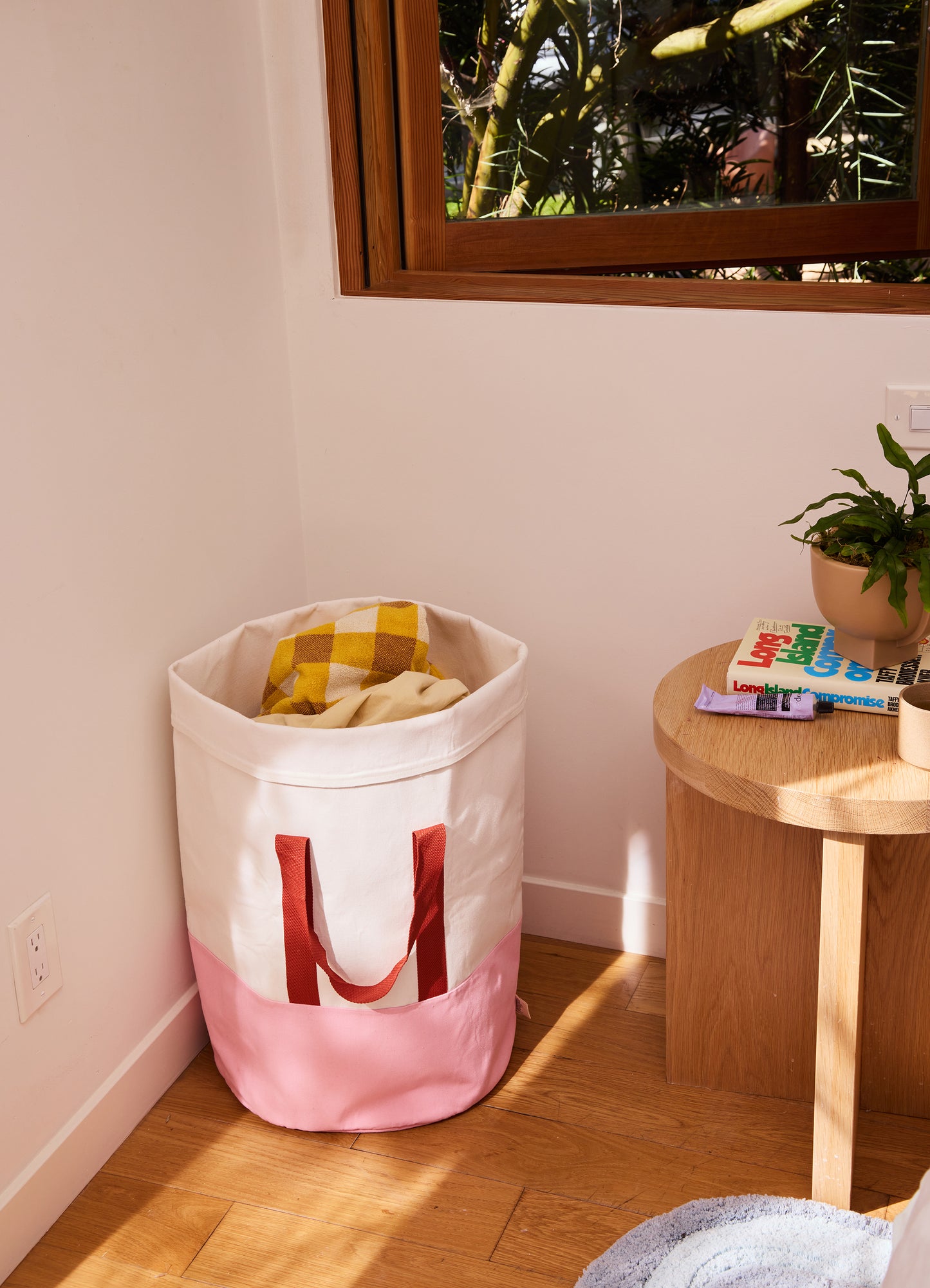 pink and cream laundry hamper in a bedroom setting under a window.