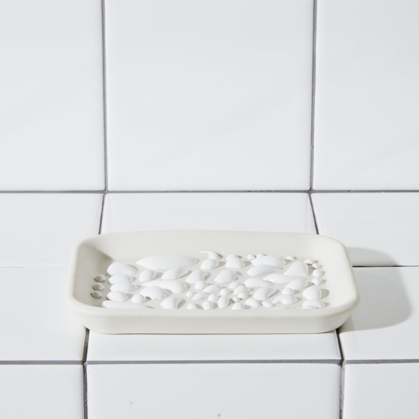 White textured soap dish shot in white tiled bathtub.
