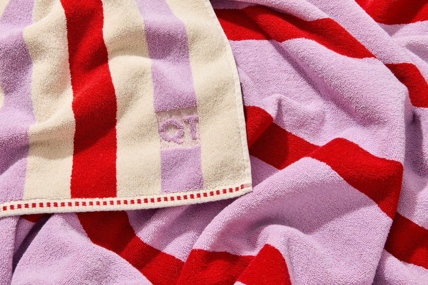 Close up shot of corner of catalina bath sheet in candy, featuring embossed QT logo.
