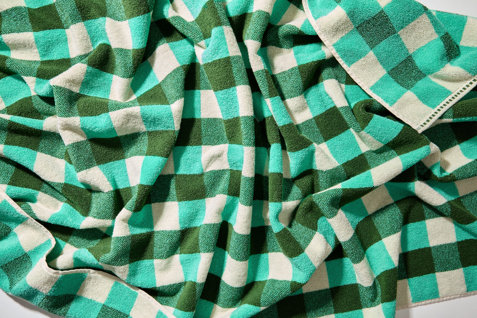 Detail view of tam bath sheet scrunched up to show checks in pine, jade, and cream.