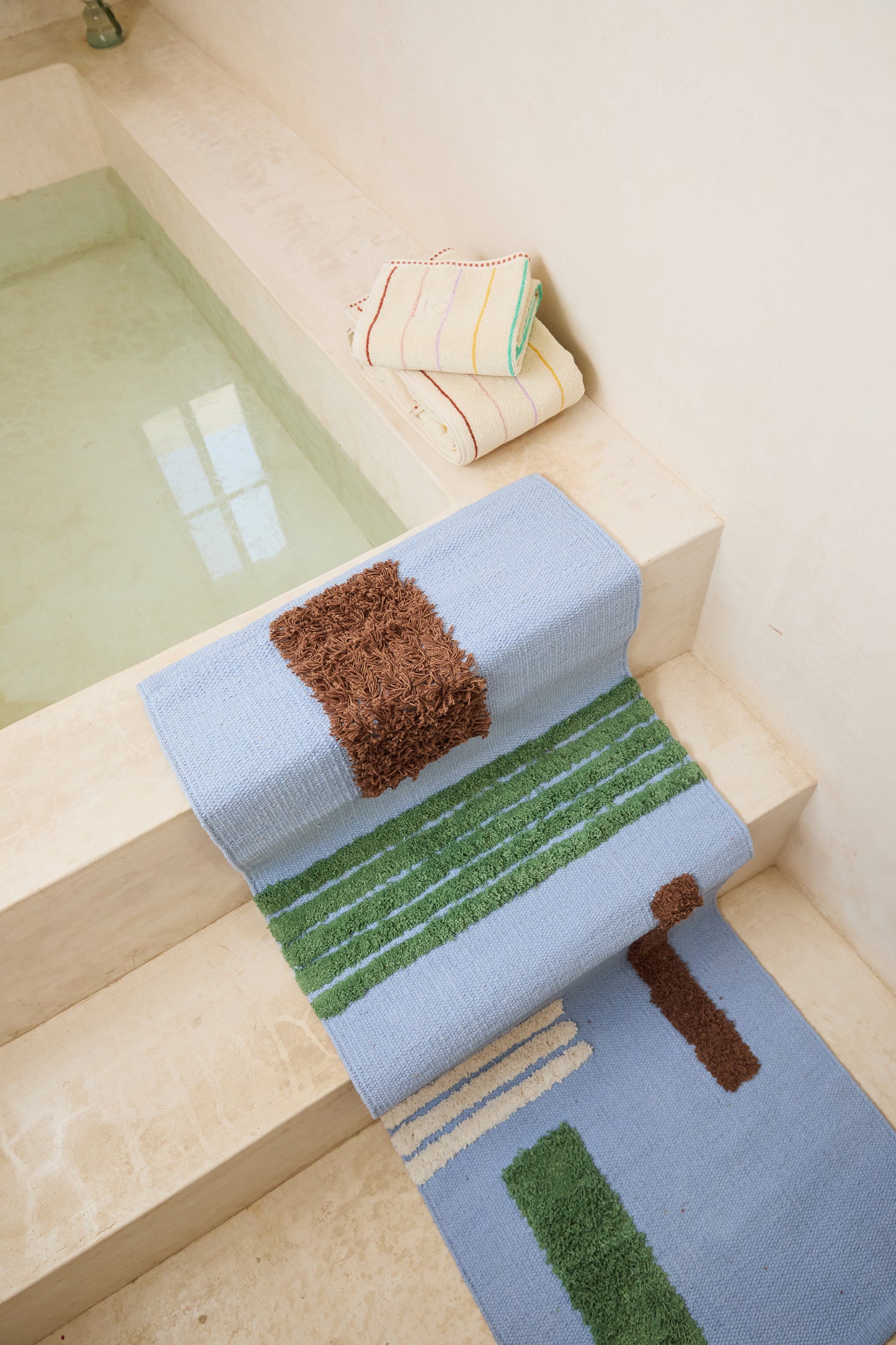 blue striped reyes rug in bathroom laying over steps of bath tub. styled with striped prism towels.