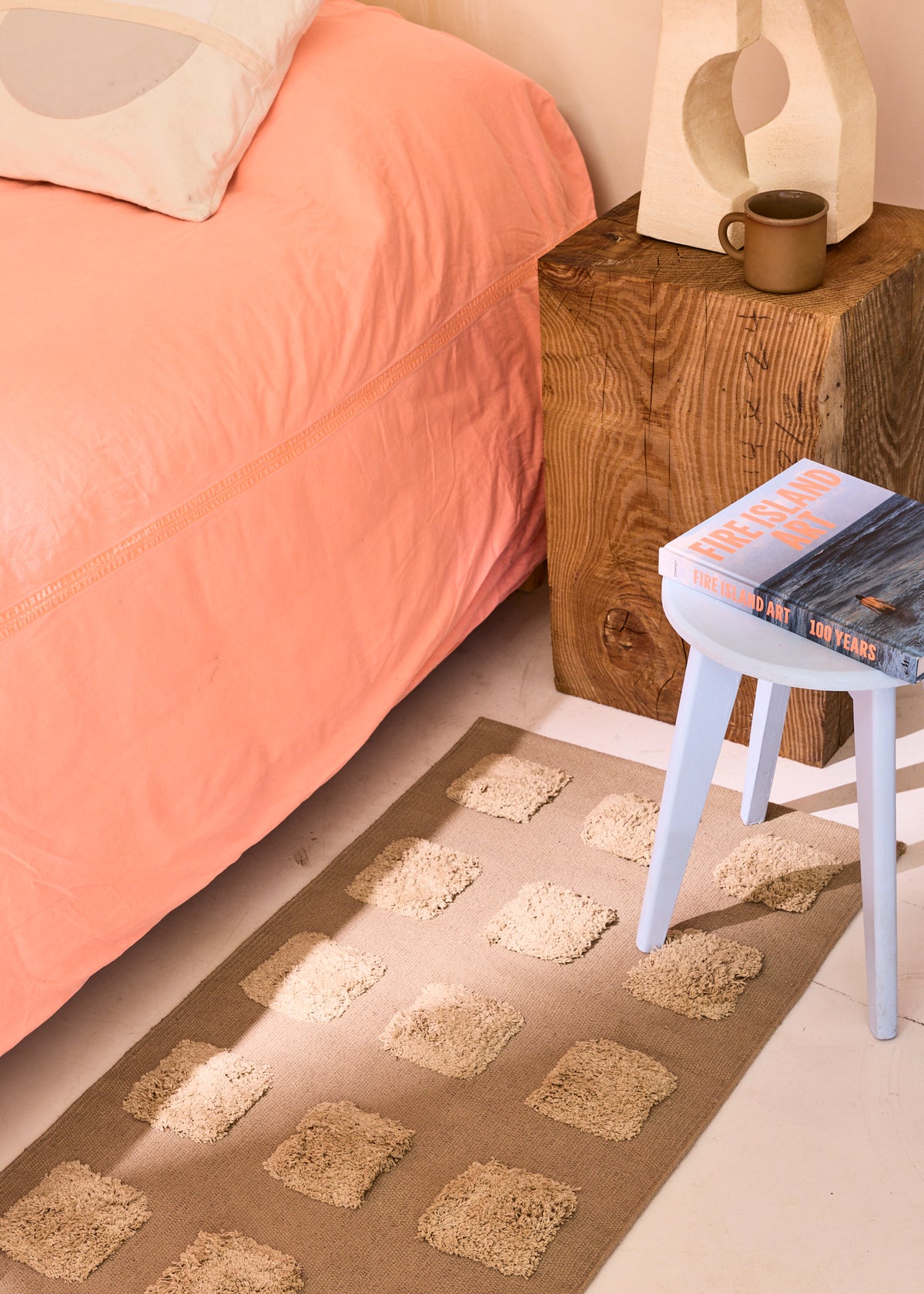 khaki rug with square texture next to a bed with orange duvet.