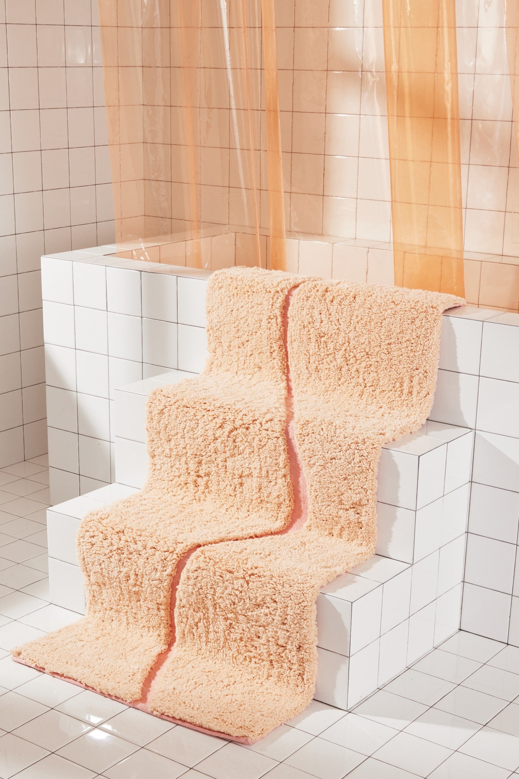 Peach bath mat in 56"x22" size with pink curvy path stripe contrast styled down the stairs of a white tiled bathtub.