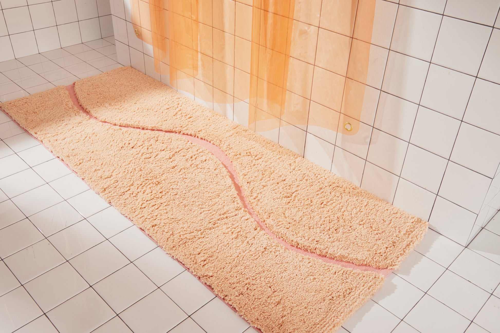 Full view of peach bath mat in 56"x22" size with pink curvy path stripe contrast shot styled in a white tiled bathroom.