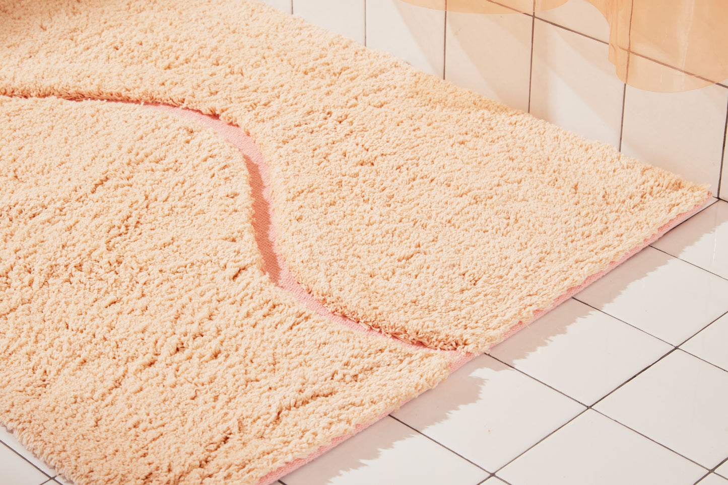 Close up view of peach bath mat in 21"x31" size with pink curvy path stripe contrast shot styled in a white tiled bathroom.